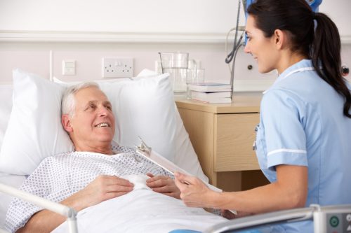 Smiling nurse with a chart sitting with a reclined elderly patient in a health care facility.