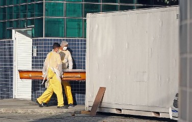 Agentes funerários levam caixão para retirar corpo em contêiner frigorífico, no Rio de Janeiro 