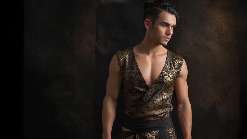 Cinematic hyperrealistic full-body ultra realistic ultra detailed wide shot of a handsome young man with black hair tied in a bun, wearing a sleeveless black outfit with golden lace, bare chest, brown batik sarong, and royal jewelry, riding a colossal Garuda with radiant golden feathers and royal ornaments, facing a terrifying giant creature in a rocky green valley. The creature is full-body, massive and muscular, with long wavy black hair, sharp fangs, bare chest, wearing a brown batik sarong and royal jewelry, exuding power and menace. Behind the giant, a full-body army of similar terrifying beings stands in formation, filling the valley with an overwhelming presence. The Garuda spreads its wings wide, golden feathers rendered in intricate detail, jewelry sparkling realistically. Ultra detailed textures on skin, muscles, feathers, fabrics, and rocky terrain. Dramatic cinematic lighting, mist rising between green hills and stone cliffs, epic atmosphere, mythical and legendary tone, ultra sharp 8K realism.