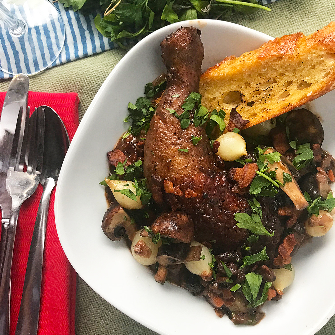 a shallow bowl filled with a roasted chicken thigh, veggies, and crusty bread a shallow bowl filled with a roasted chicken thigh, veggies, and crusty bread