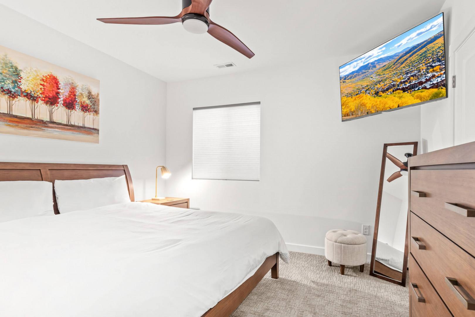 Sink into crisp white linens in your serene bedroom, where a ceiling fan keeps you cool and warm artwork adds a cozy touch. Natural light, a stylish dresser, and thoughtful decor complete your peaceful retreat.