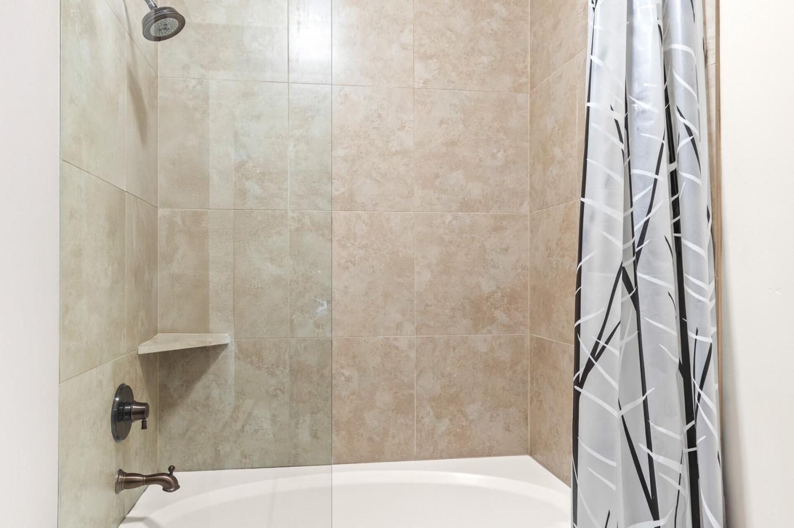 Step into your spacious tiled shower with modern fixtures and thoughtful built-in shelf for your toiletries.