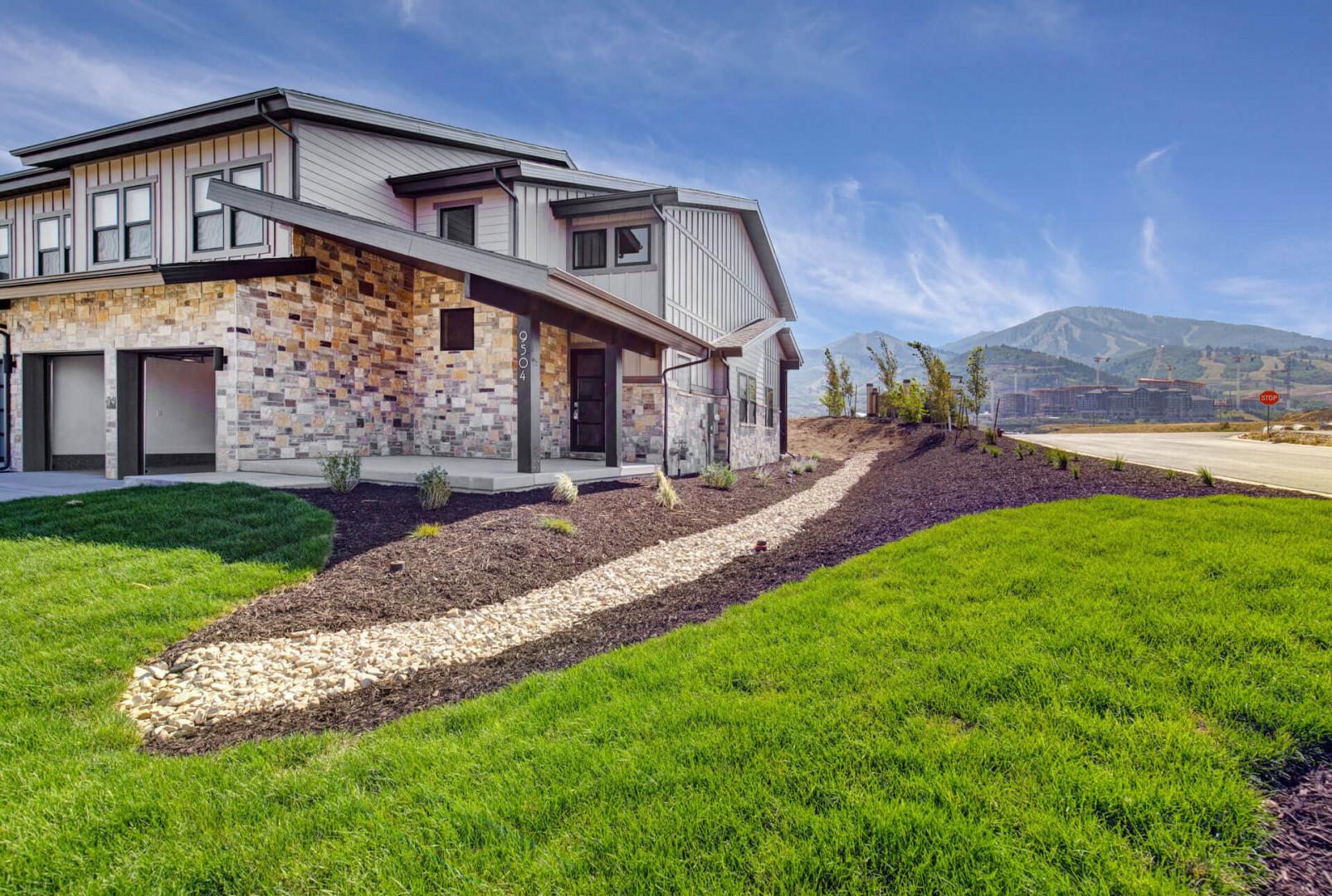 A striking mountain rental with modern architecture, natural stone accents, and thoughtfully landscaped grounds set against scenic mountain peaks.