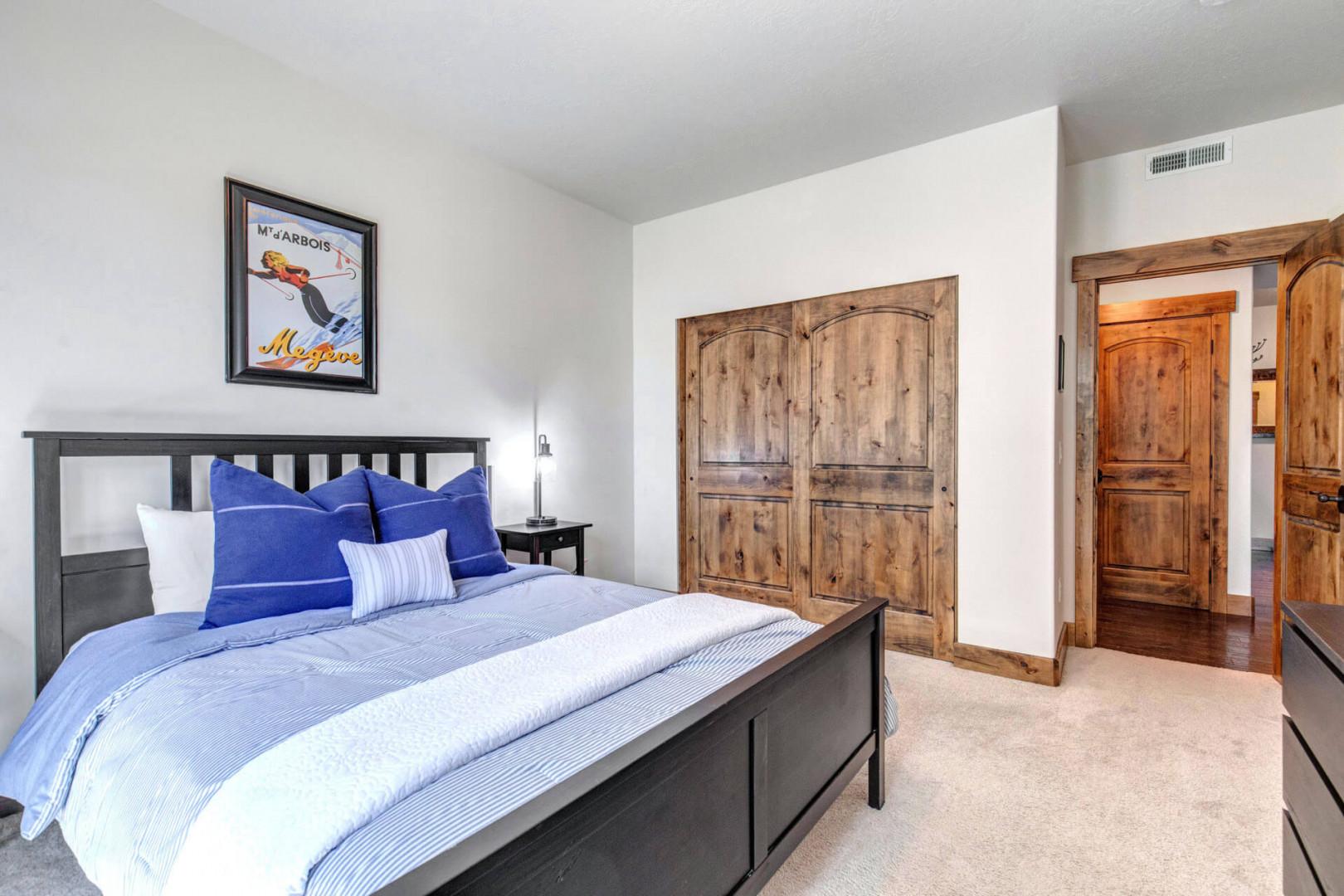 Unwind in this inviting bedroom with its plush bed dressed in crisp blue linens and cozy pillows. The rustic wooden wardrobe adds mountain charm, while soft carpet underfoot ensures comfort.