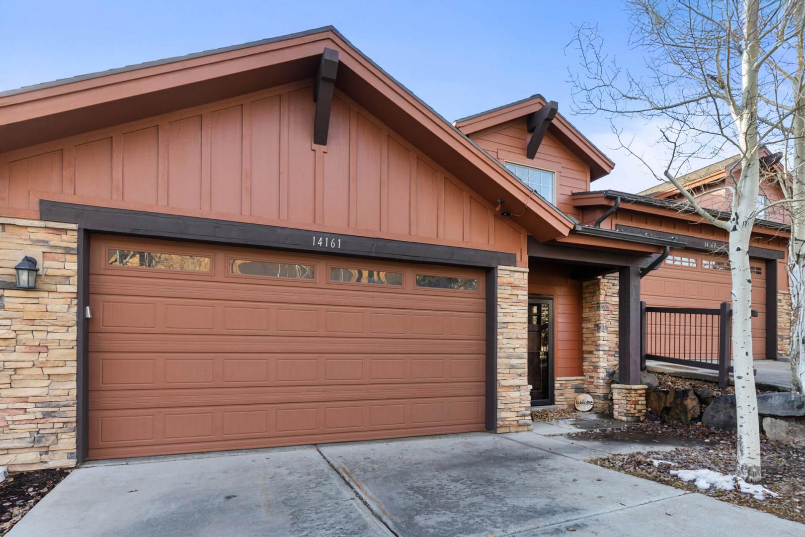 Modern mountain home featuring warm wood and stone exterior with convenient garage access and scenic surroundings.