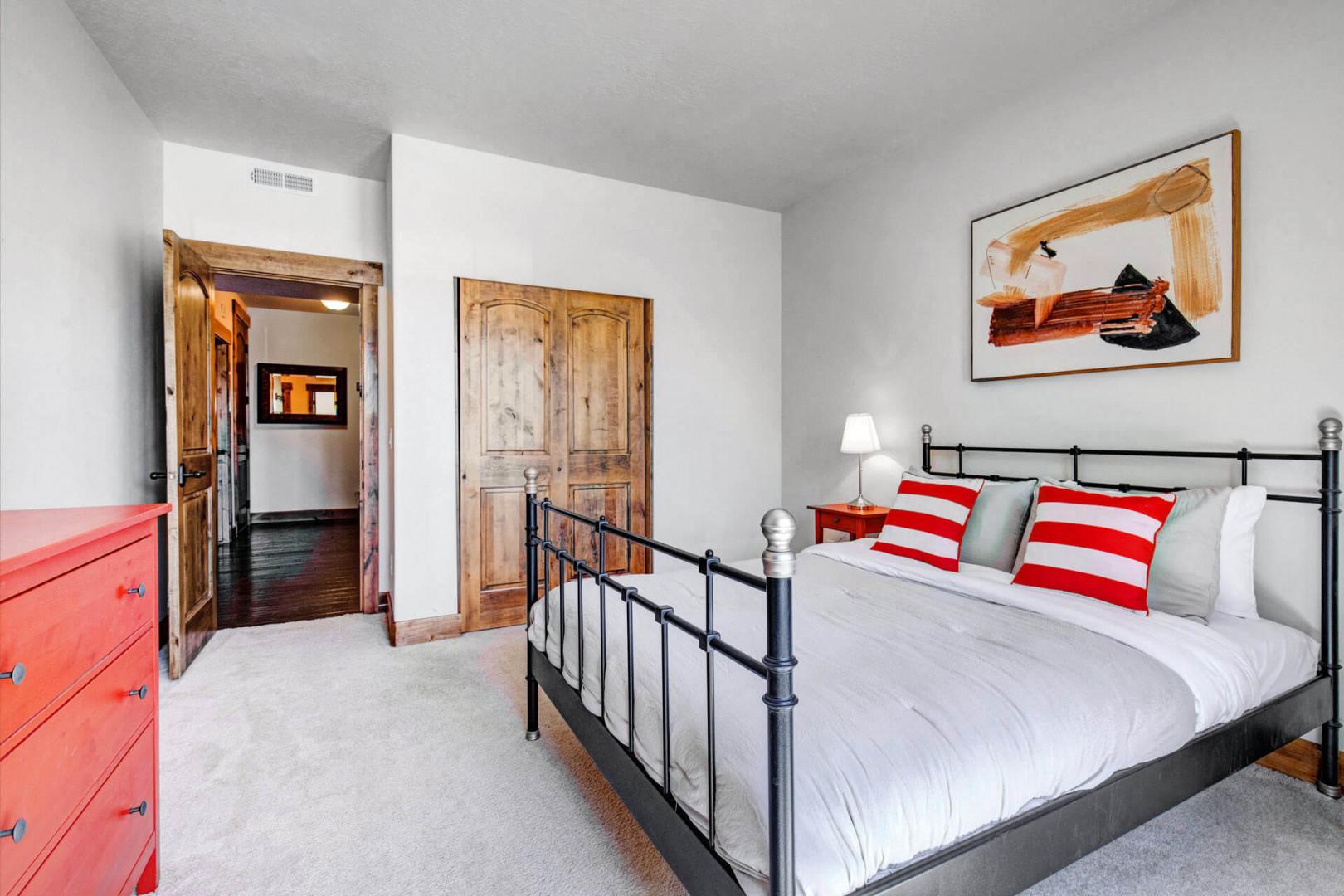Sink into crisp white linens and cheerful red-striped pillows in your restful bedroom, where rustic wooden doors and vibrant artwork add character to your mountain getaway.