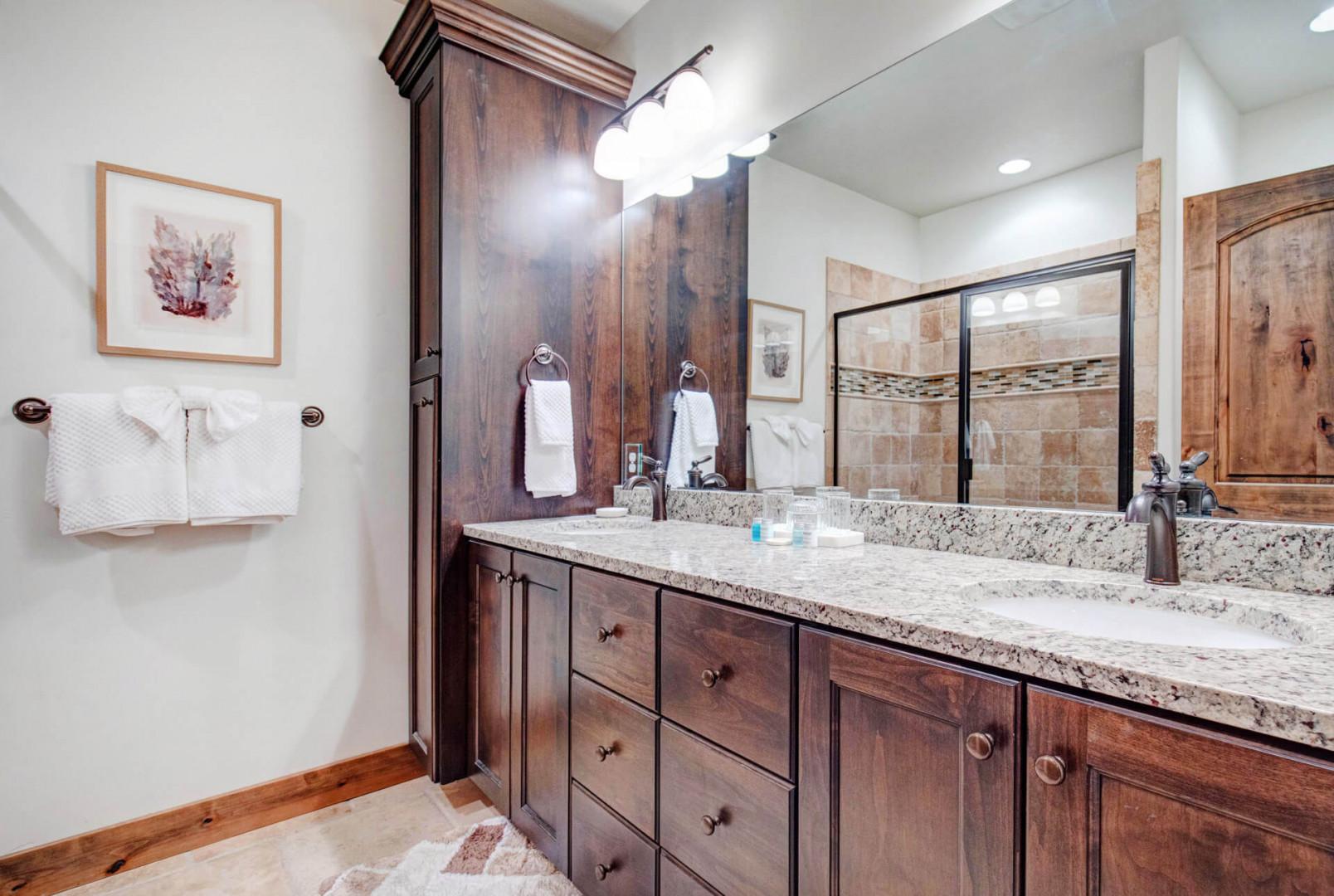 Step into your private bathroom featuring rich wood cabinetry, gleaming granite counters, and a spacious walk-in shower. Fresh towels await your arrival, and thoughtful details create a warm, spa-like atmosphere for unwinding.