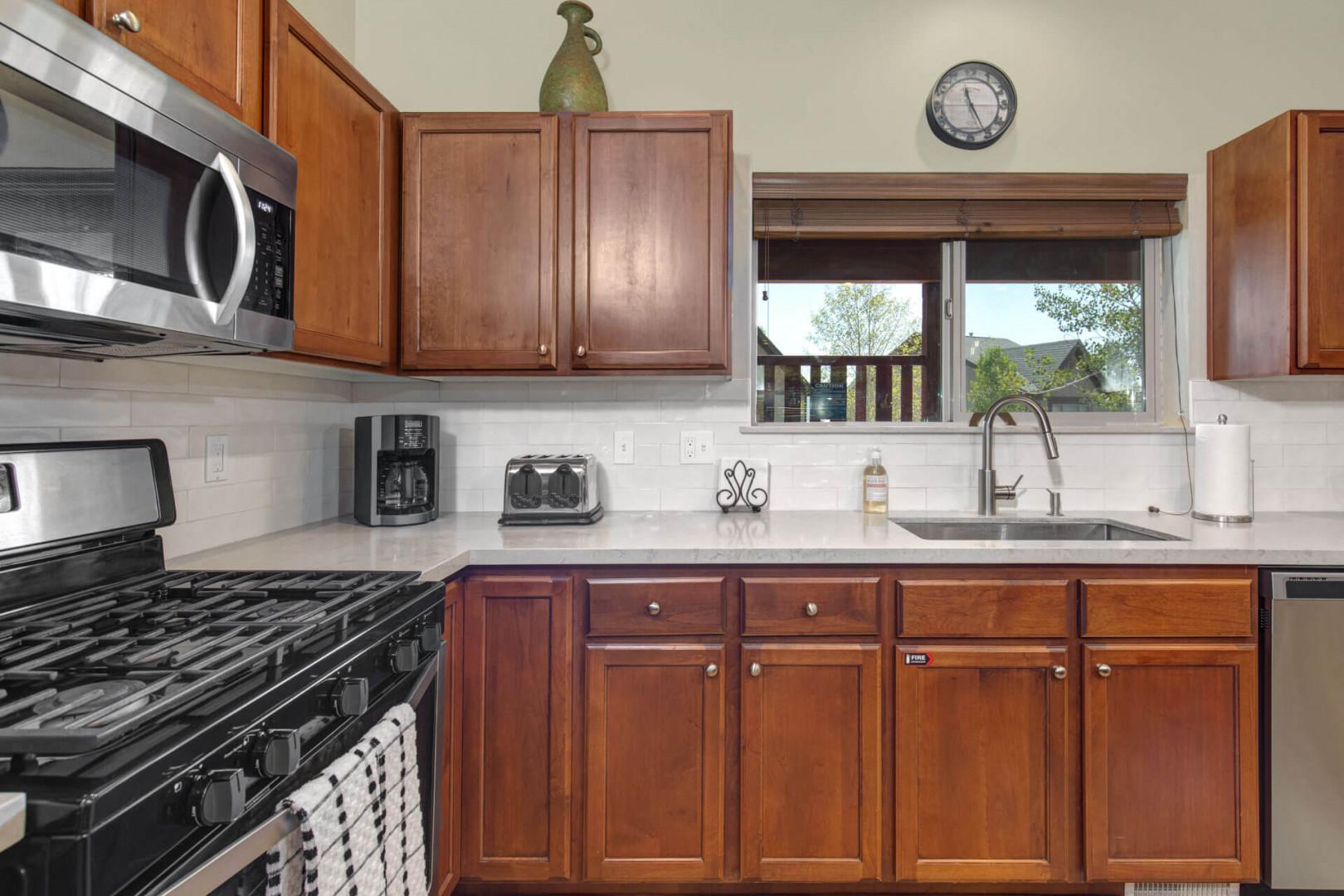 Your fully-equipped kitchen awaits with warm wood cabinetry, modern appliances, and mountain views through the window.