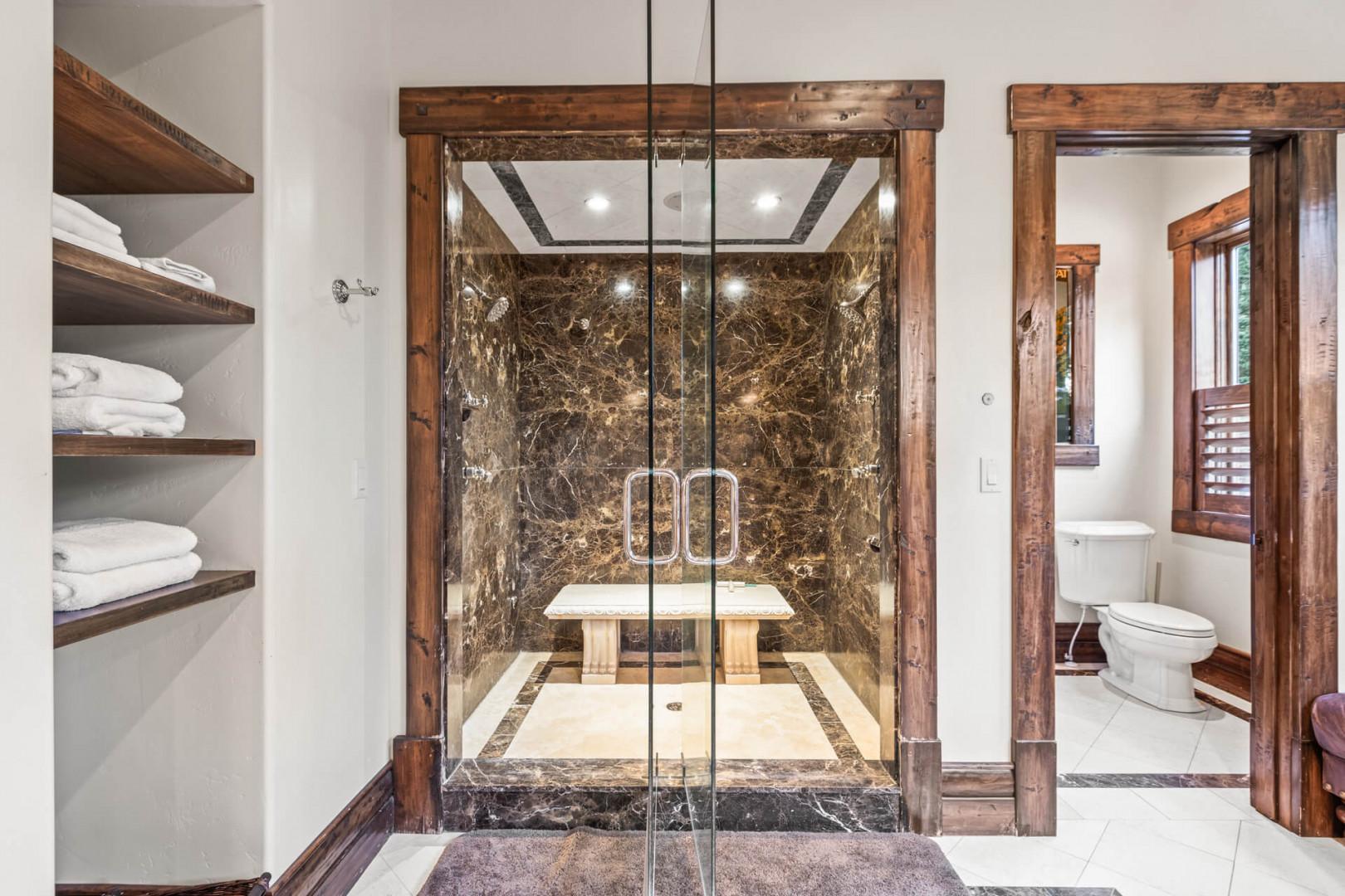 Luxurious bathroom with dual shower heads, bench, and toilet.