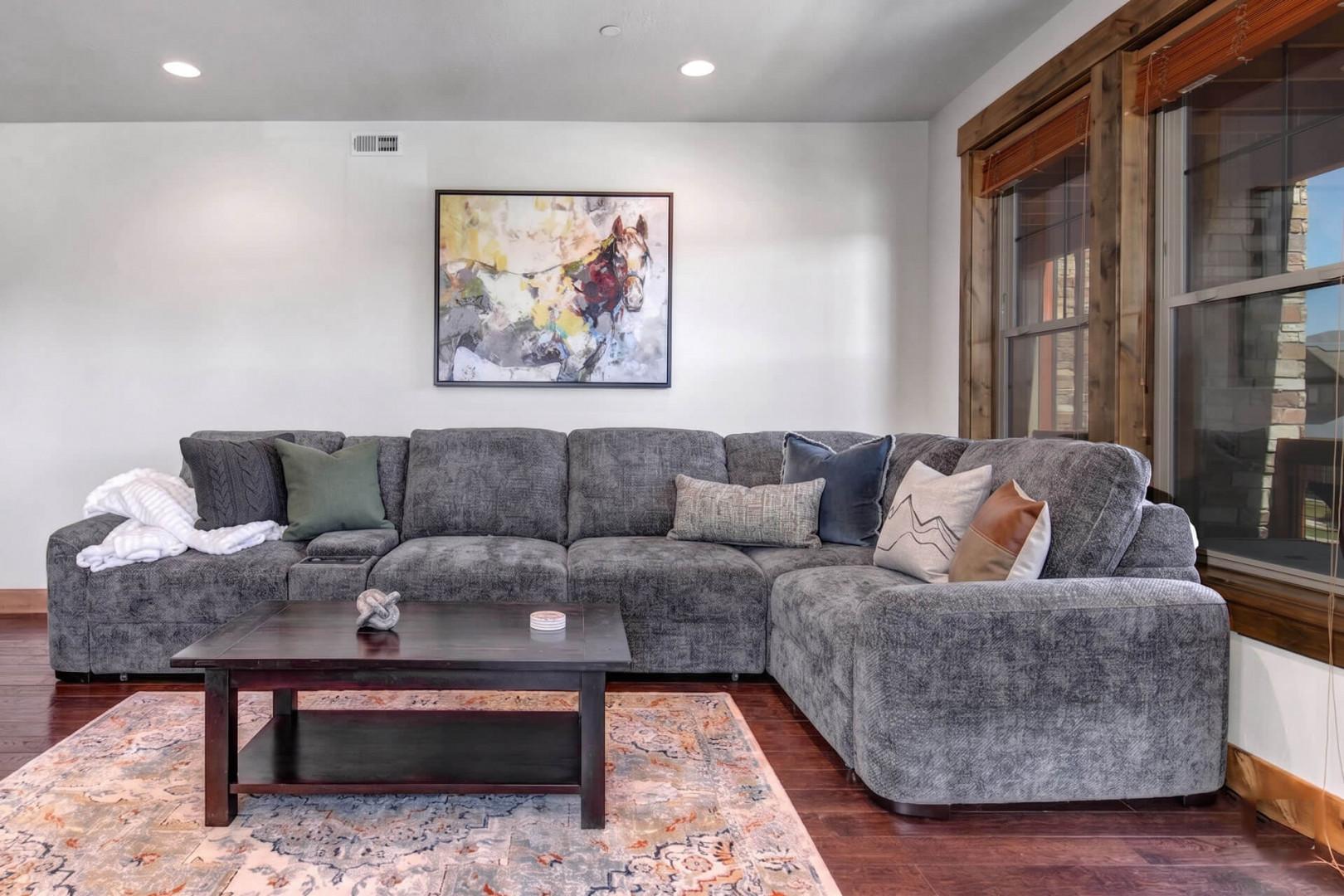 Sink into the plush gray sectional and unwind in your spacious living room, where natural light pours through rustic wood-framed windows and contemporary art adds a splash of color to your mountain retreat.