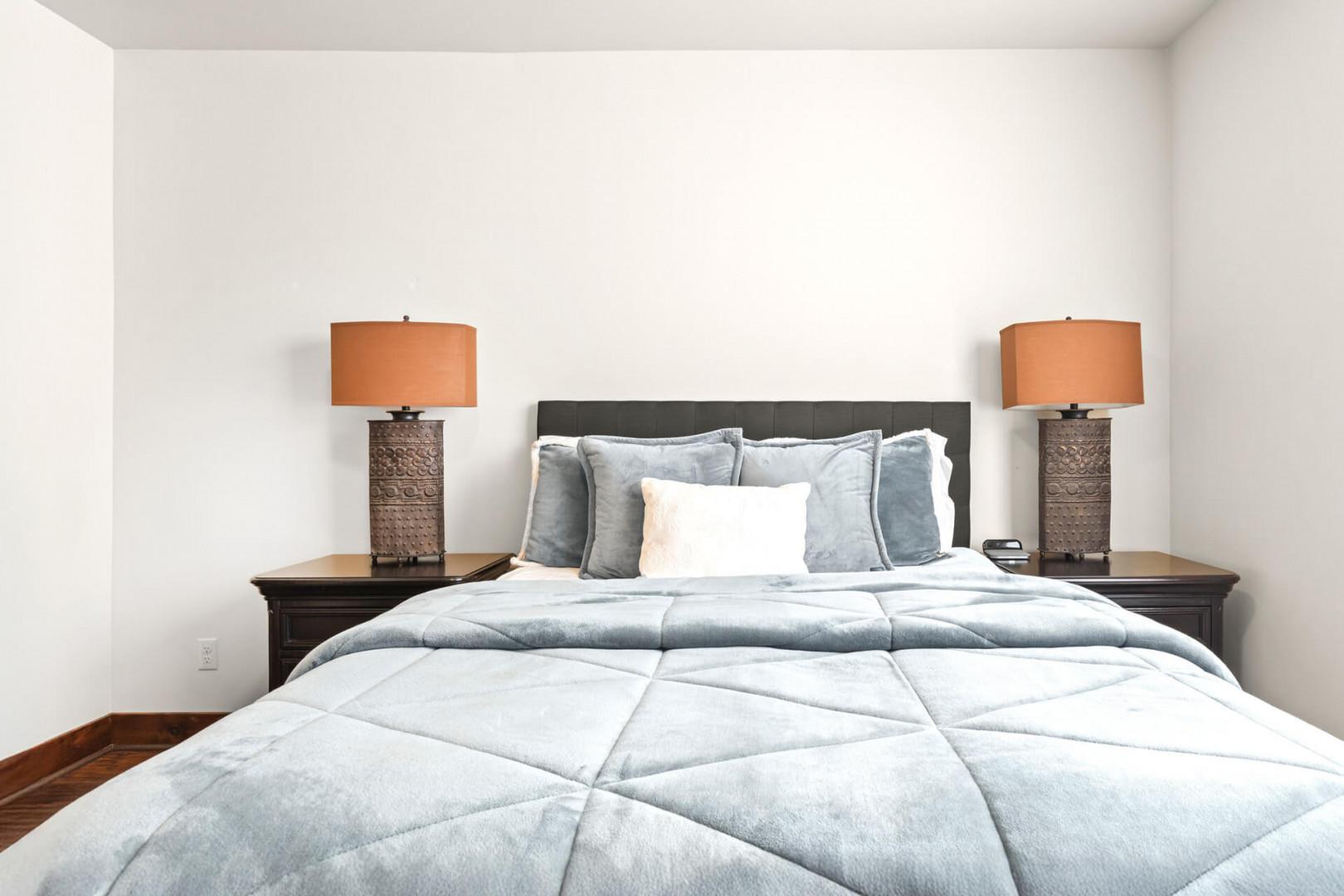 Sink into this cozy bedroom where soft blue linens and warm bedside lighting create your perfect retreat for restful nights.