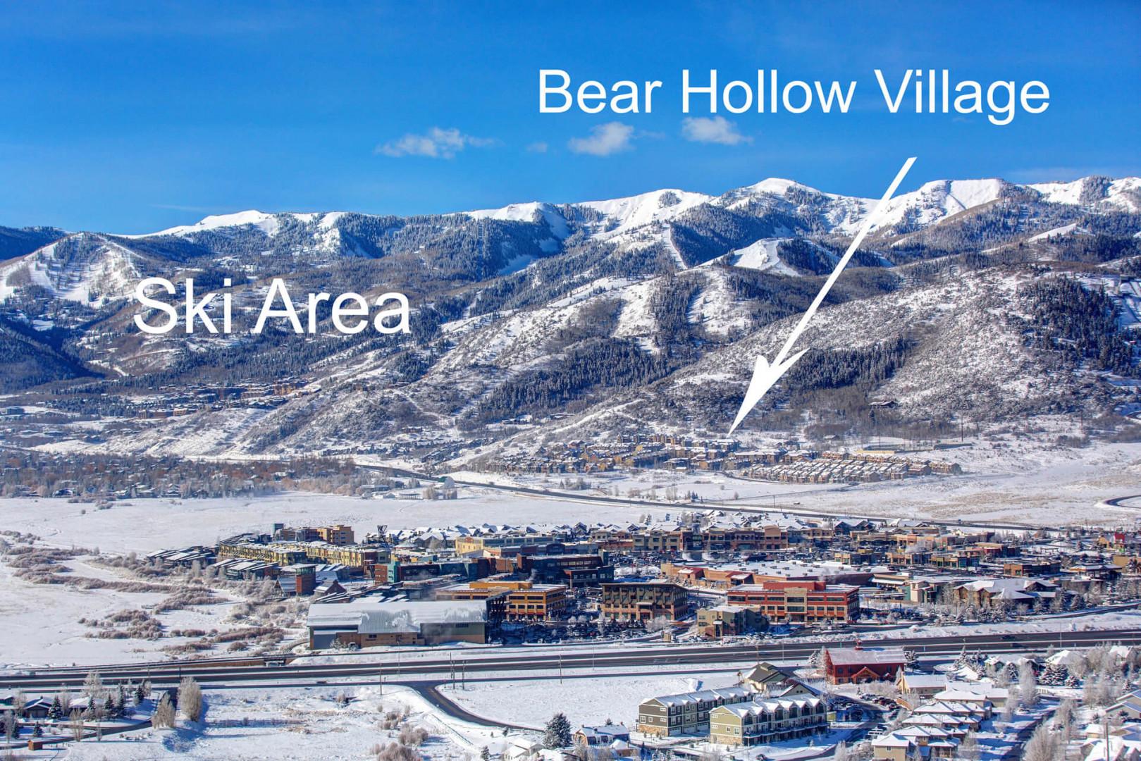 Aerial view of Bear Hollow Village nestled below snow-covered mountains and ski slopes in a picturesque winter resort town.