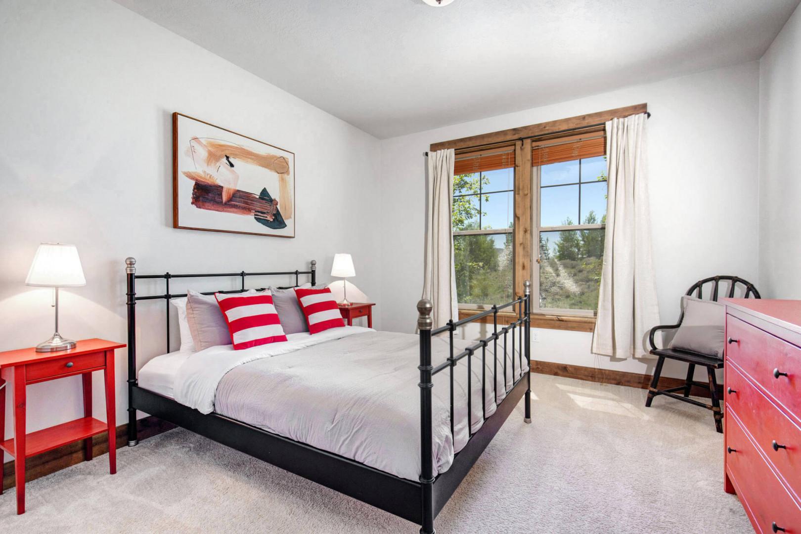 Rest easy in your cozy bedroom, where natural light streams through beautiful wooden-framed windows and reveals scenic views beyond. Crisp linens and cheerful pops of color create a welcoming retreat.