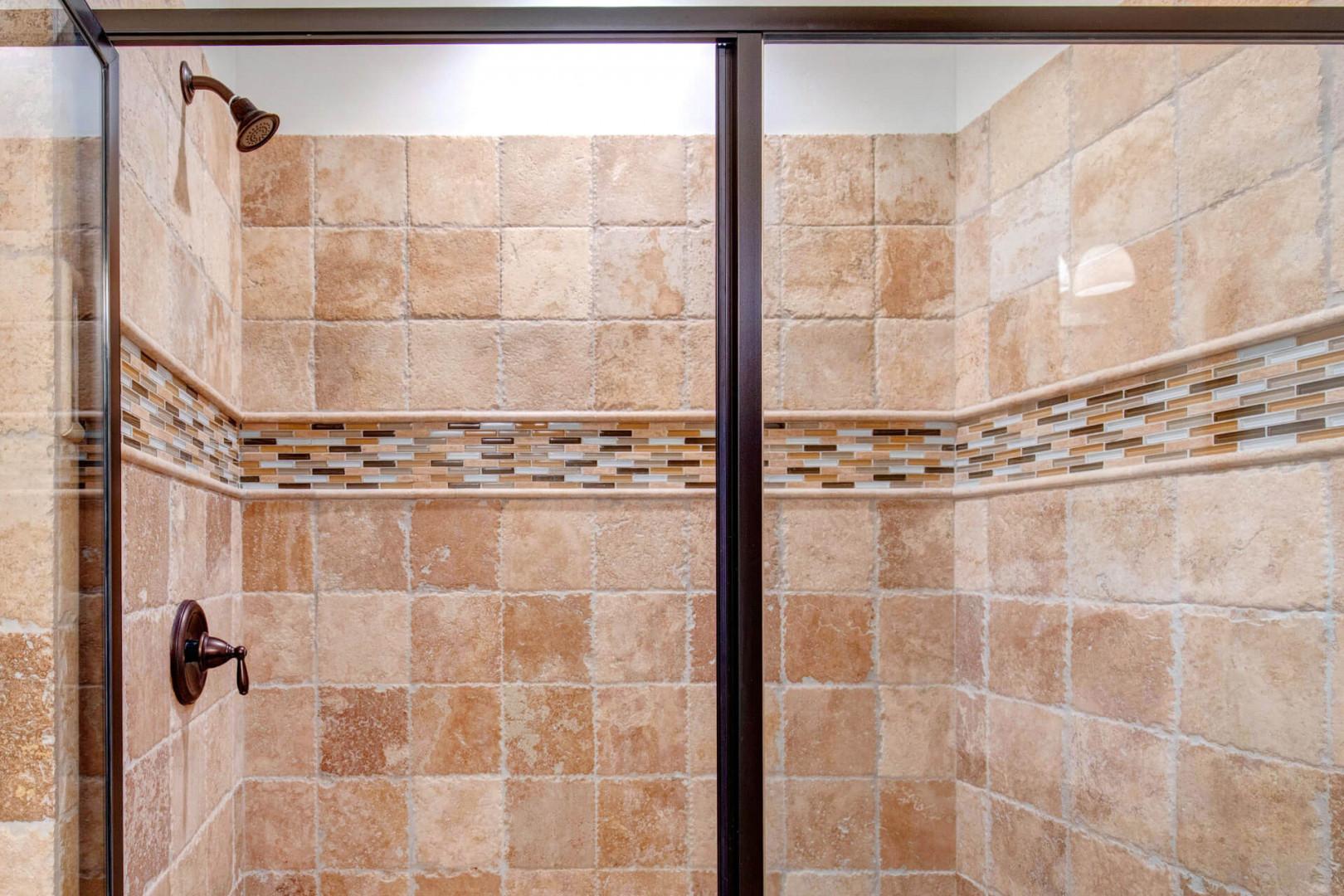 Step into your private retreat with a beautifully tiled walk-in shower featuring warm earth tones, elegant mosaic accents, and a rainfall showerhead—your refreshing escape after a day of adventure.