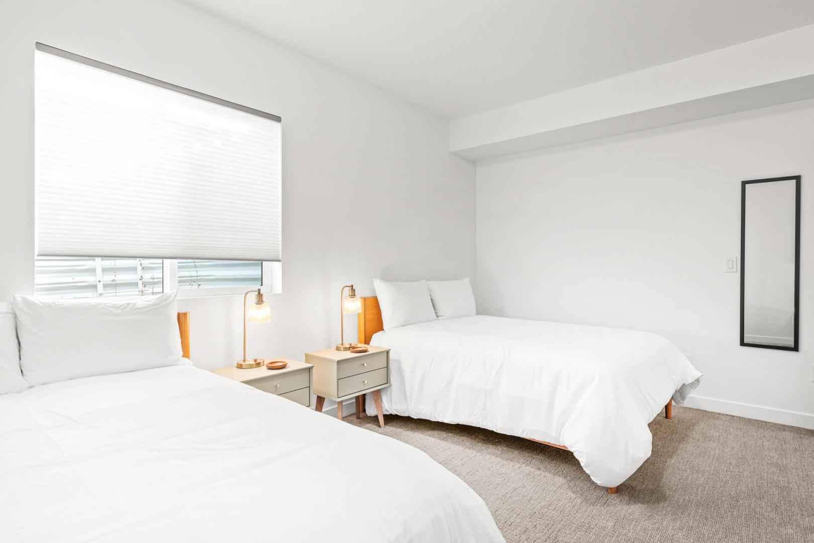 Drift off in crisp white linens as natural light fills your serene bedroom. Two comfortable beds, stylish lamps, and calming décor create your perfect coastal retreat.