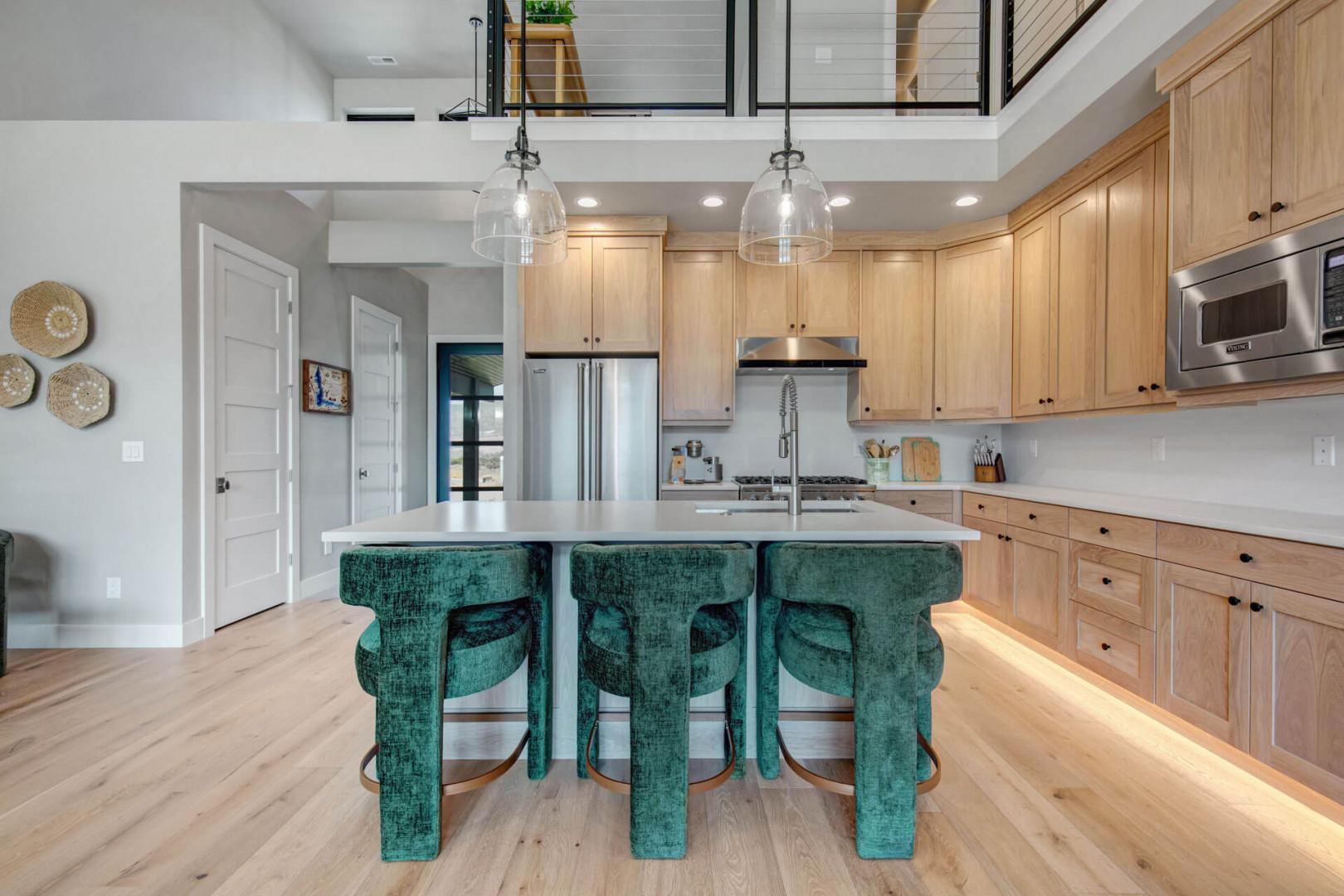 Spacious gourmet kitchen featuring natural wood cabinetry, elegant pendant lighting, and stainless appliances. The generous island with plush velvet seating is perfect for morning coffee or evening gatherings.