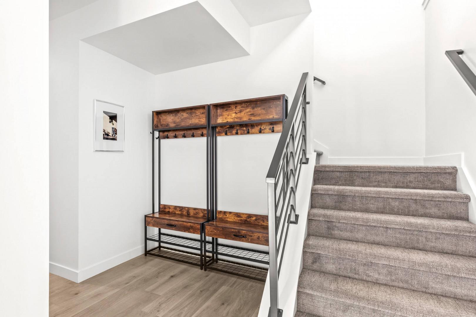 Slip off your shoes and hang your coat in this entryway featuring custom built-in storage. The modern rustic bench and hooks make settling in effortless, while the bright, open stairwell adds a welcoming sense of space.