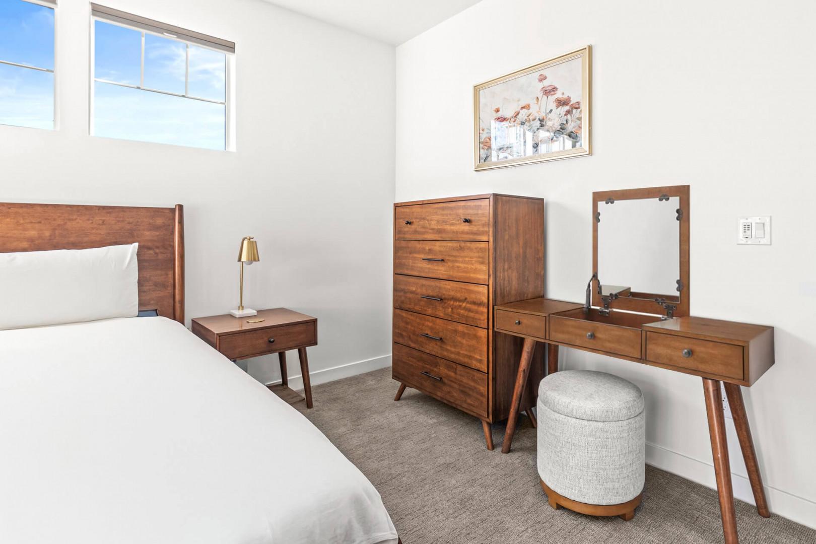 Your peaceful bedroom retreat features mid-century modern furnishings, plush bedding, and a vanity for getting ready. Natural light fills the space, creating a bright, welcoming atmosphere for restful nights.