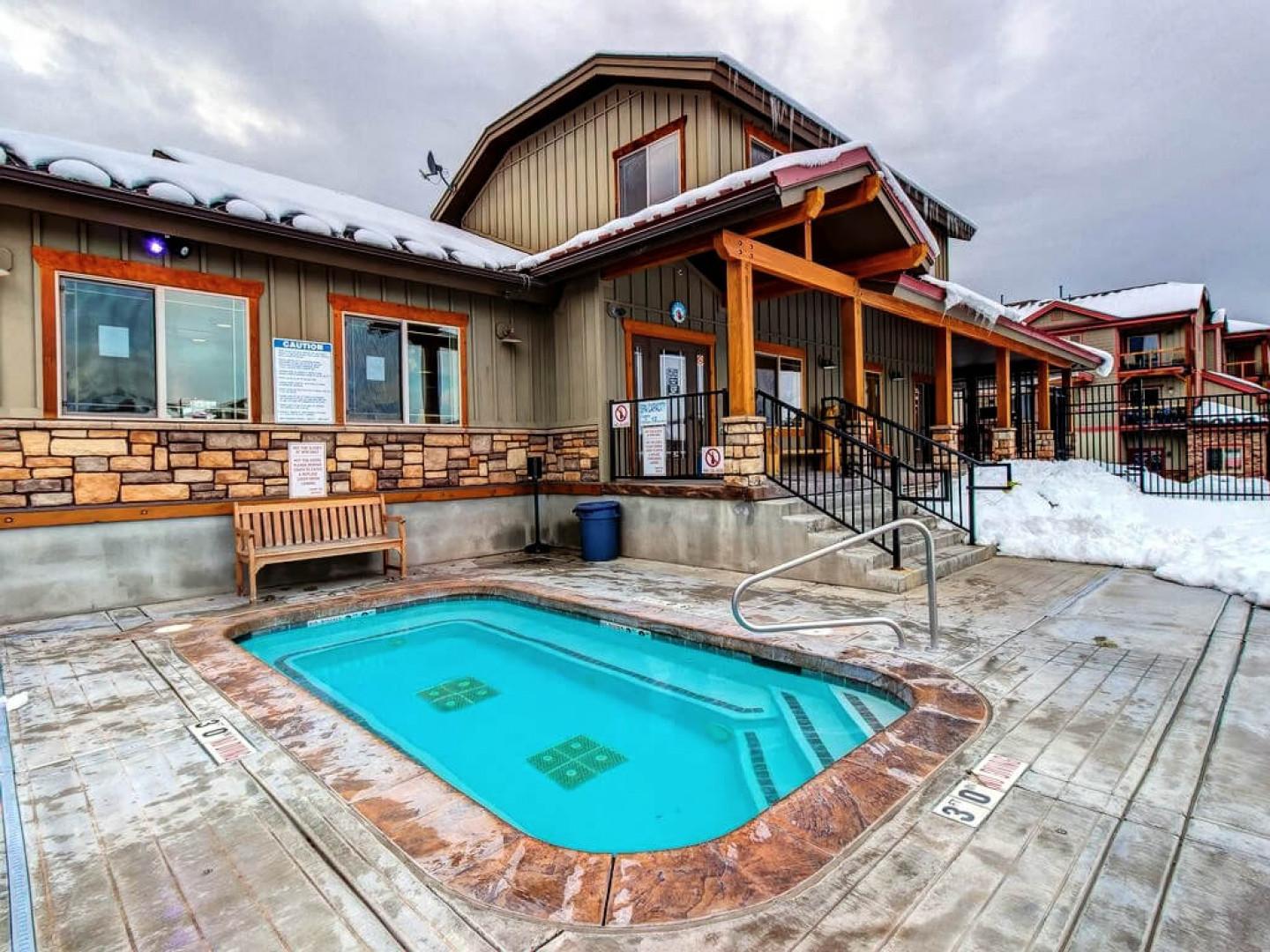 A heated outdoor pool nestled against rustic mountain architecture, surrounded by snow-dusted rooflines and peaceful alpine scenery—perfect for warming up after a day on the slopes.