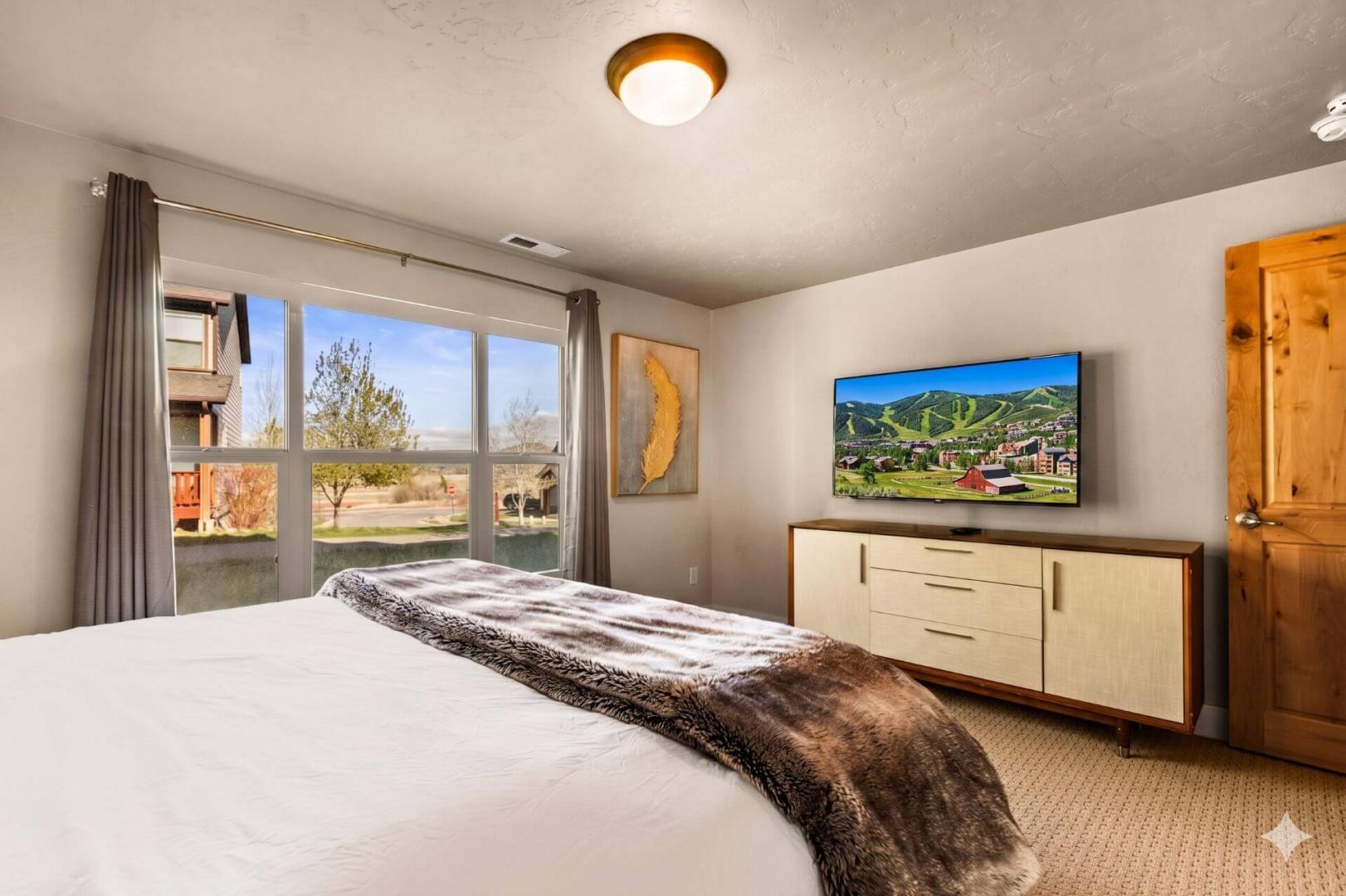 Your peaceful bedroom features a comfortable bed and modern TV, with natural light streaming through large windows for a restful stay.