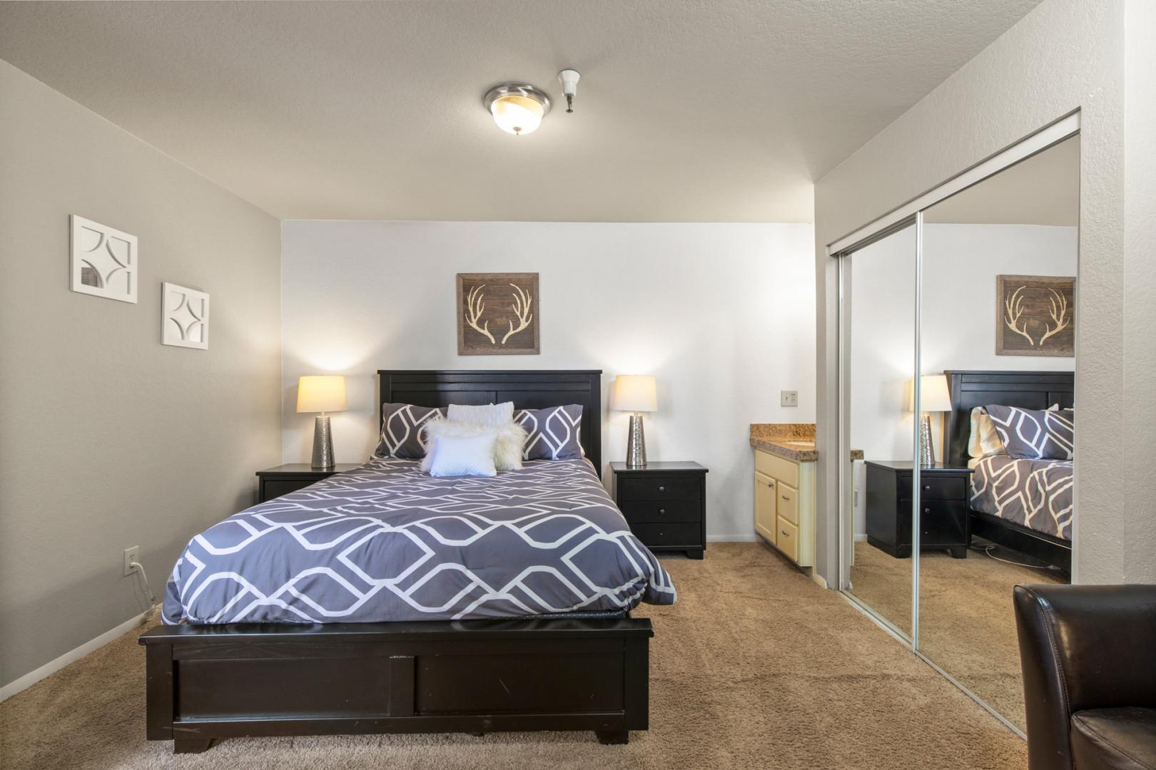 Cozy queen bed beside a clothes closet with a full-body mirror.