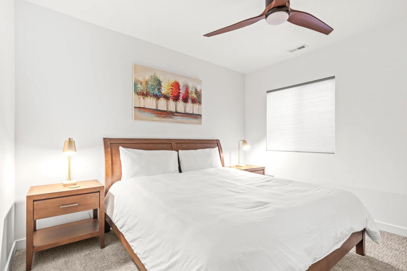 Drift off in crisp white linens under a modern ceiling fan. Natural light filters through your window, while bedside lamps offer a warm glow for evening reading.