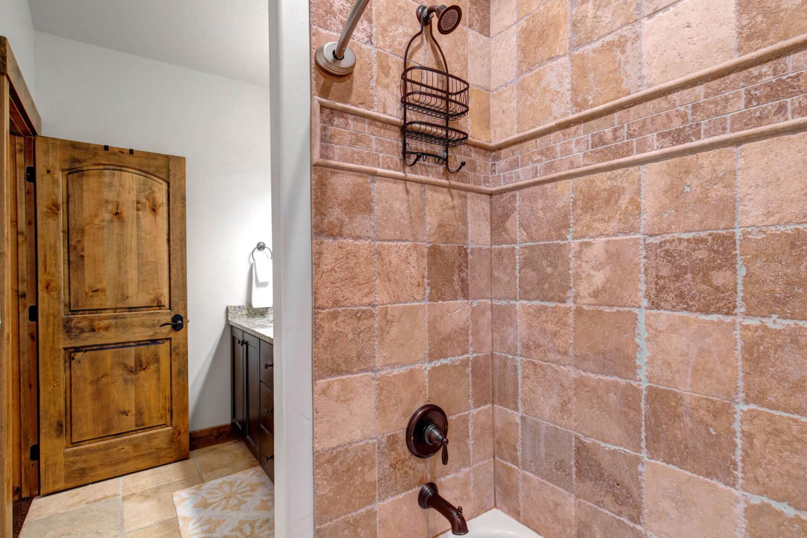 Step into a bathroom featuring warm terracotta tile, dual showerheads with a handy caddy, and sleek bronze fixtures—your own refreshing retreat awaits after exploring.