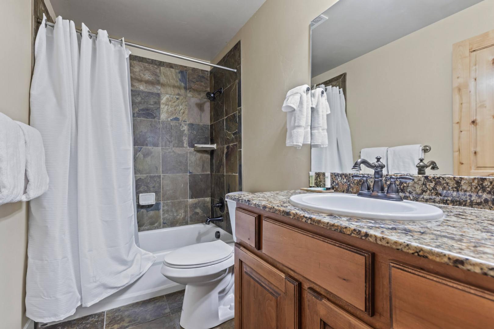 Sleek sink, mirror, toilet, and tub-shower combo in modern design.