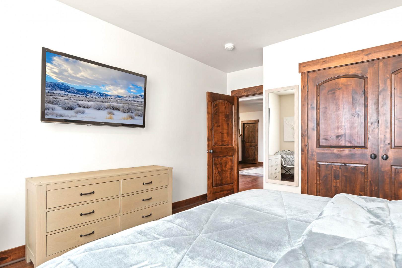 Unwind in your cozy bedroom featuring a wall-mounted TV, spacious dresser, and beautiful mountain landscape artwork to inspire peaceful dreams.