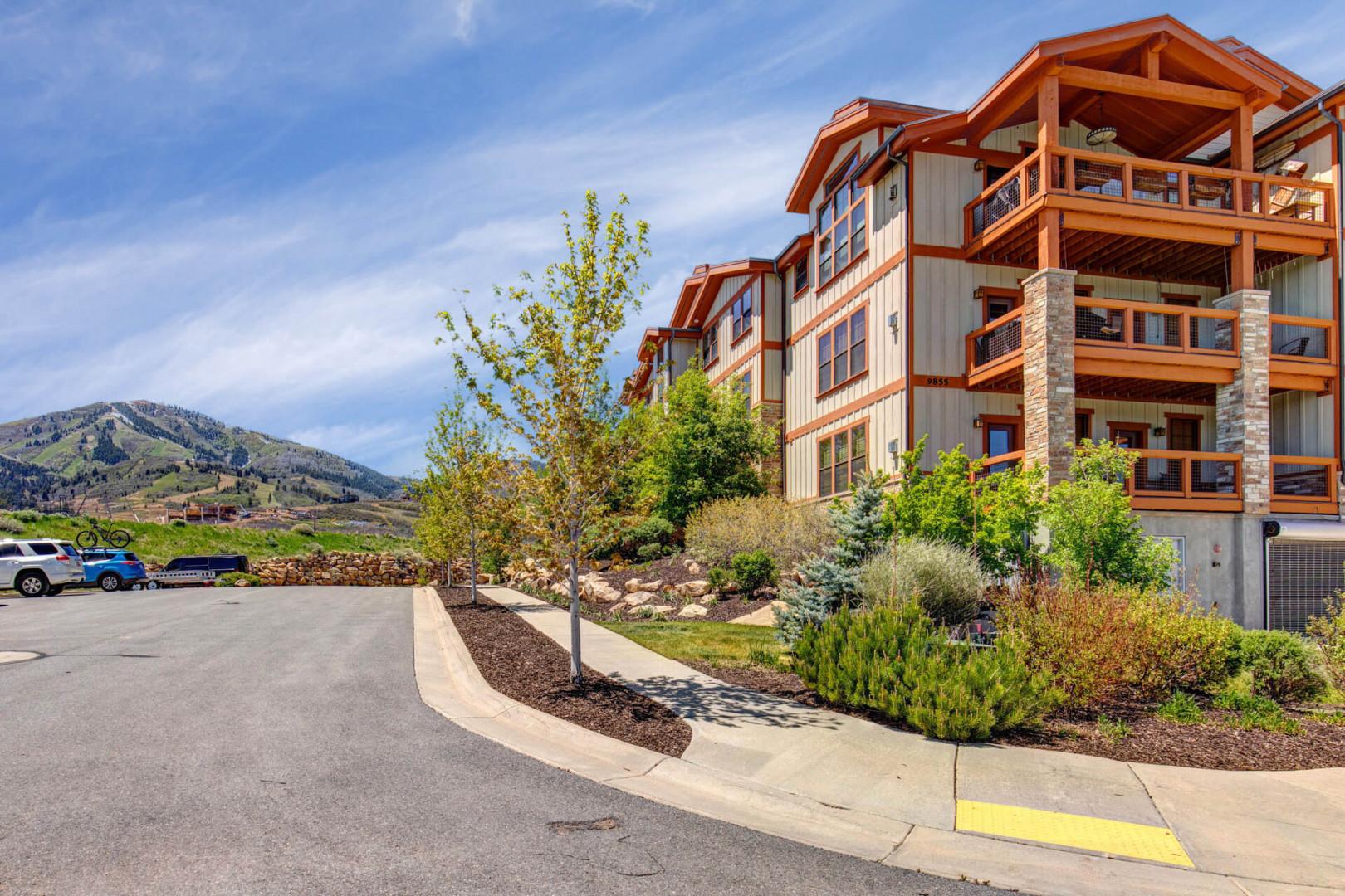 Mountain resort property with timber and stone facade, framed by landscaped gardens and mountain backdrop, offering a welcoming arrival setting.