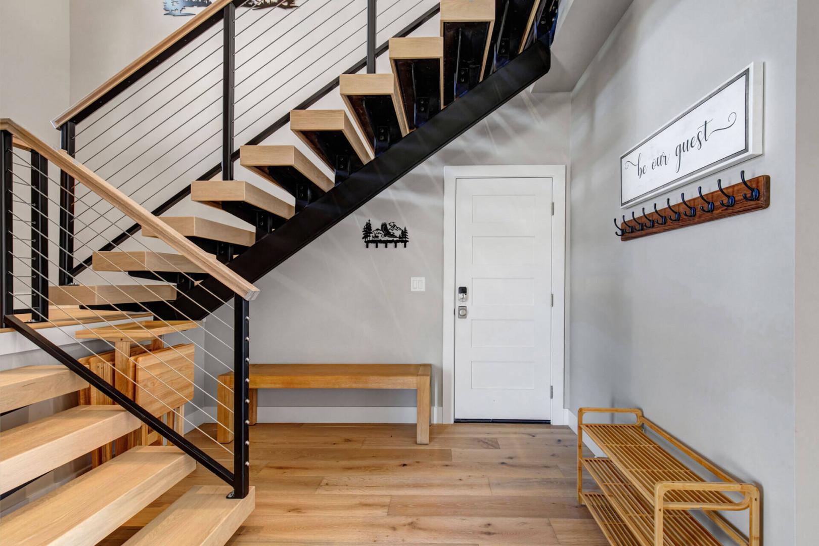 A welcoming entryway greets you with modern mountain charm—light wood floors, open stairs, and a handy bench for settling in or heading out to explore.