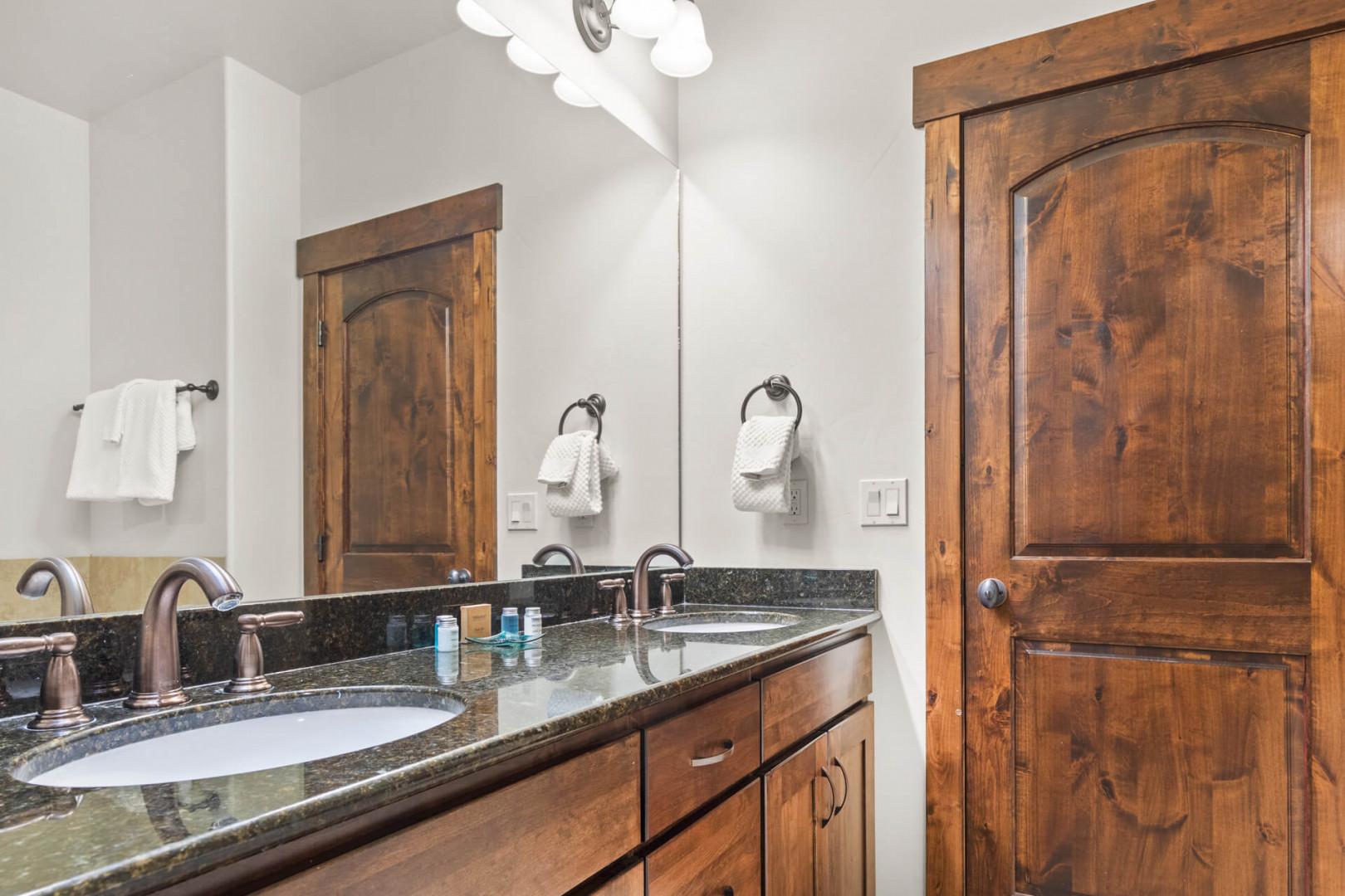 Step into your elegant bathroom with dual granite vanities, rich wood cabinetry, and pristine white towels waiting for you.