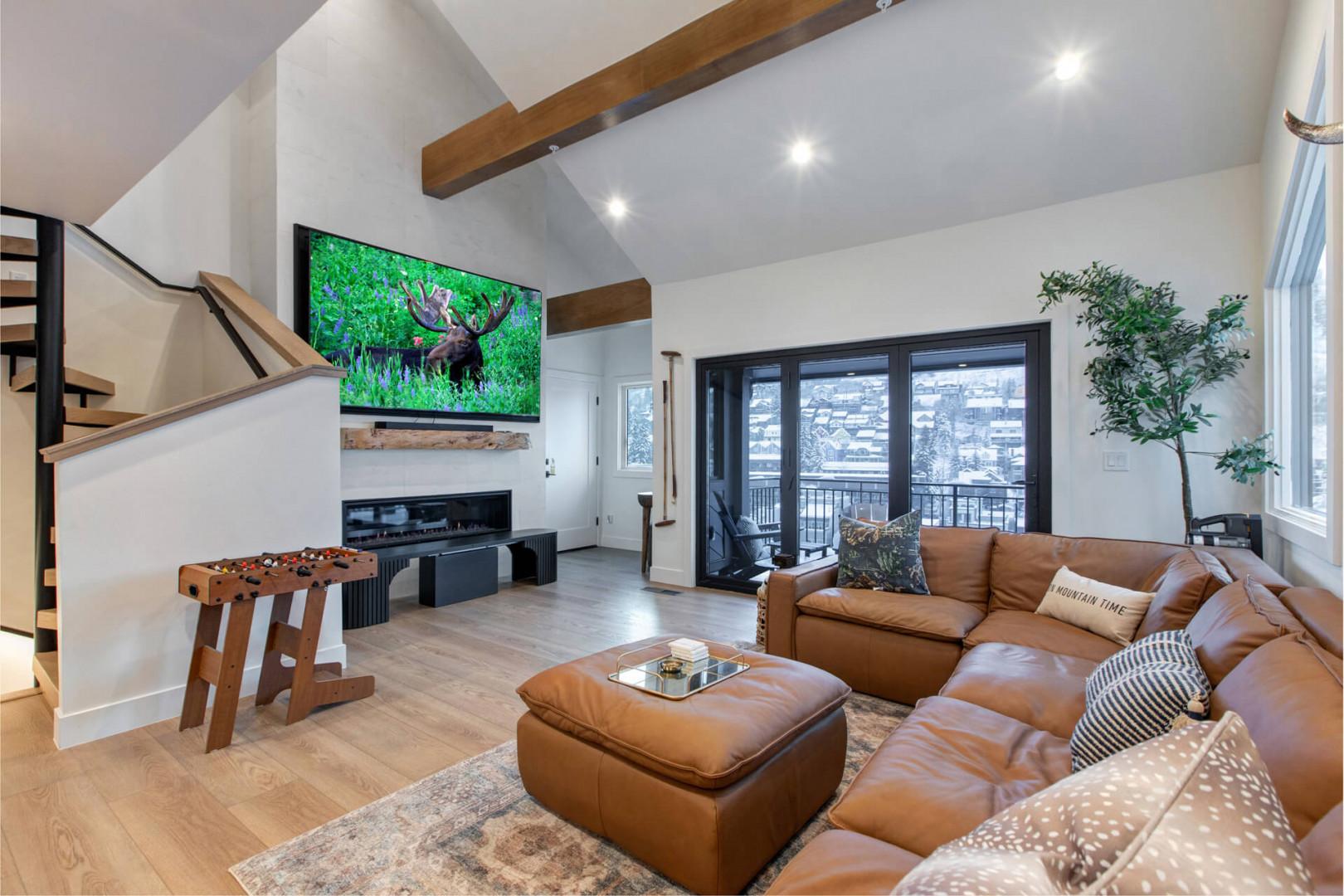 Relax in your spacious living room with leather seating, game table, and stunning mountain views through floor-to-ceiling windows.