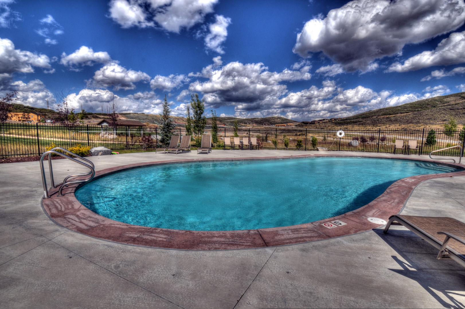 An inviting outdoor pool surrounded by lounge chairs and desert hills, offering a refreshing retreat under wide open skies in a peaceful setting.