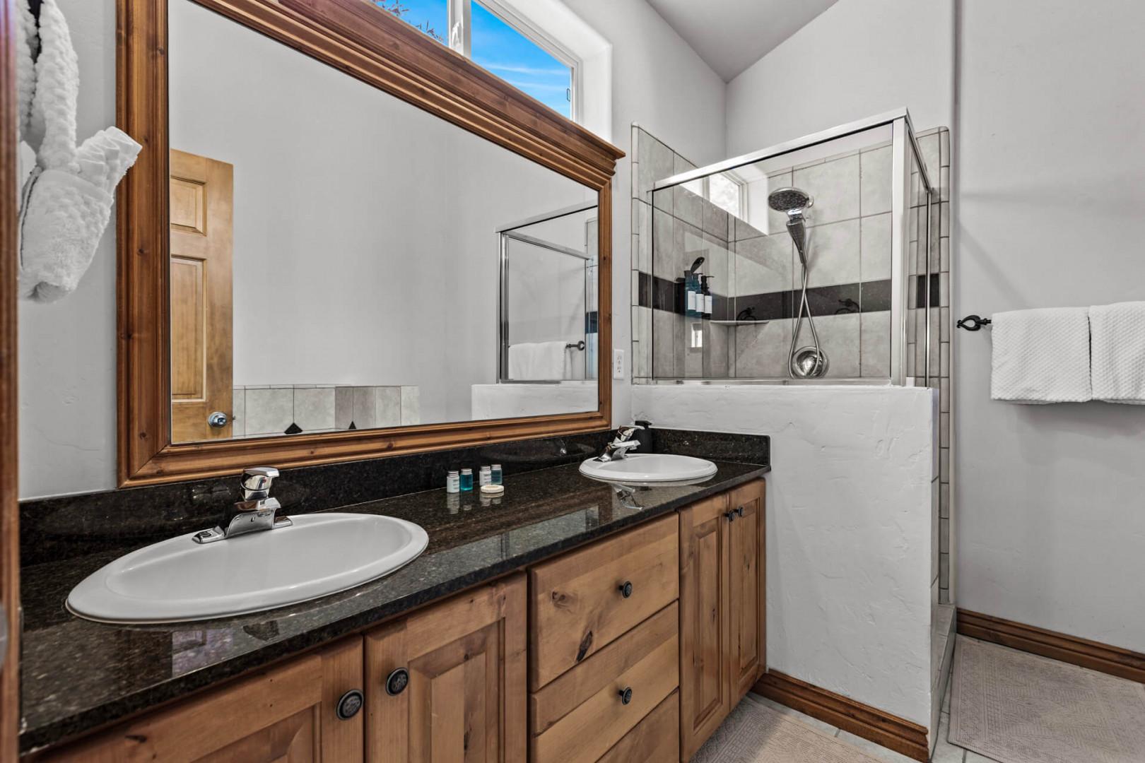 Your spacious bathroom features dual sinks with polished granite counters and a refreshing walk-in shower, all bathed in natural light from above.