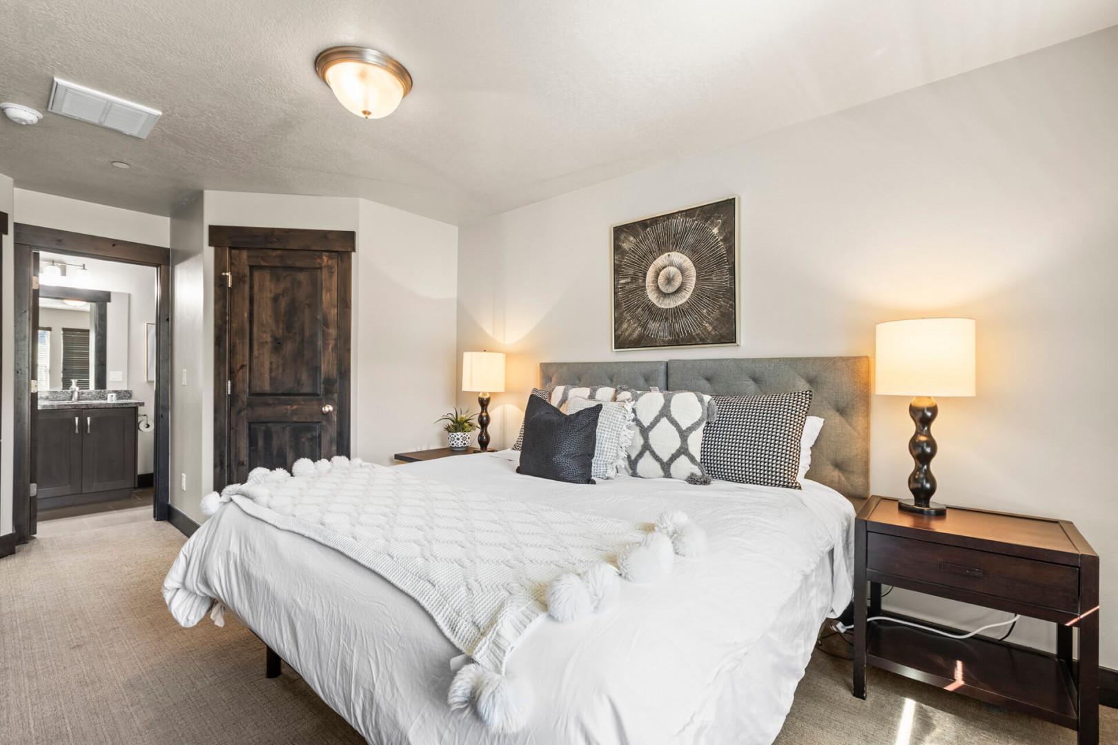 Drift into peaceful sleep in your elegantly appointed bedroom, where plush white linens and warm lighting create the perfect sanctuary for rest.