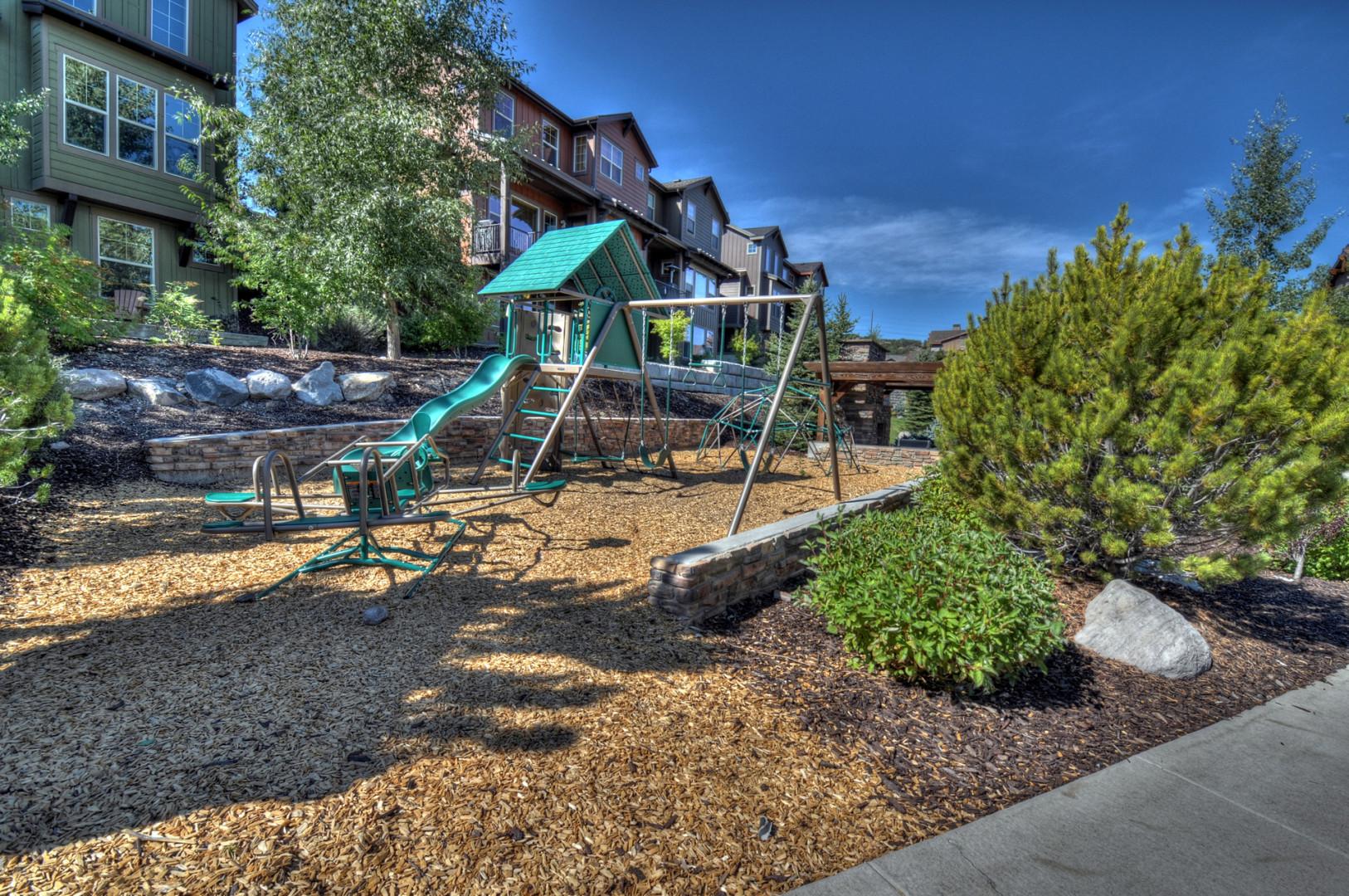 The property features a children's playground with slides and swings, nestled in landscaped grounds with native greenery. A welcoming communal space surrounded by modern residential buildings.