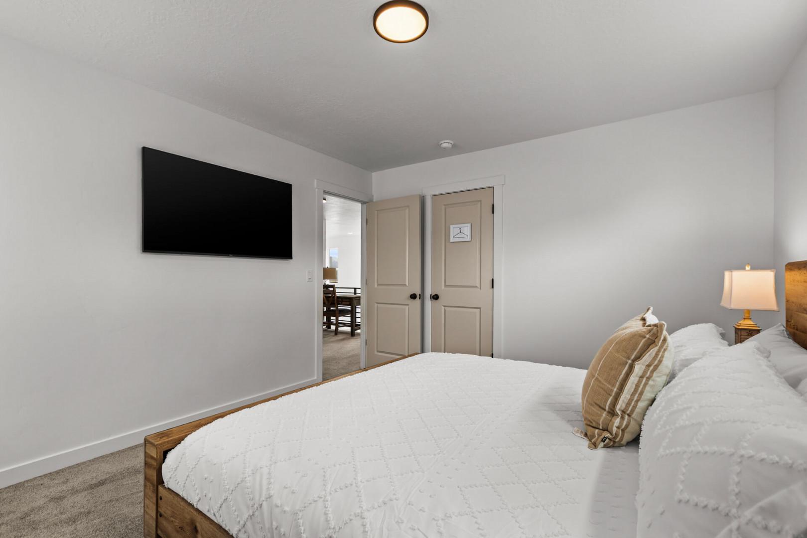 Sink into crisp white linens and unwind while watching your favorite shows on the mounted TV in this serene bedroom.
