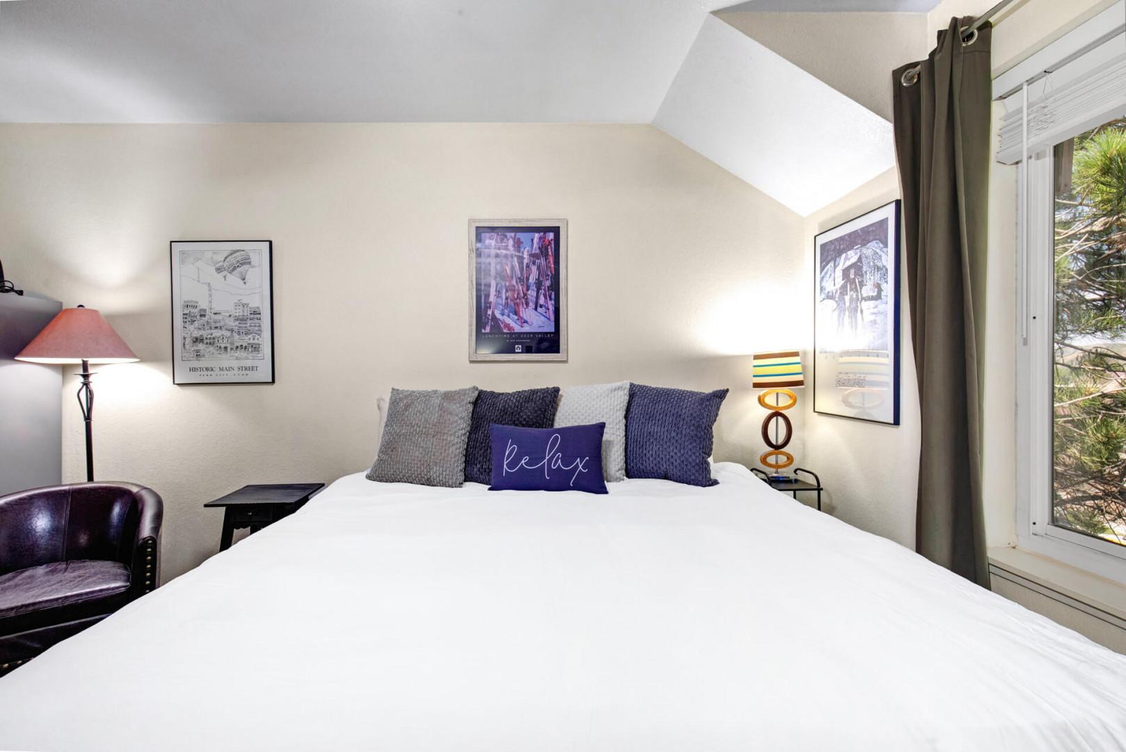 Sink into this cozy bedroom with crisp white linens, stylish accent pillows, and a skylight that fills your space with natural light. A glimpse of greenery through the window brings a touch of the outdoors in.