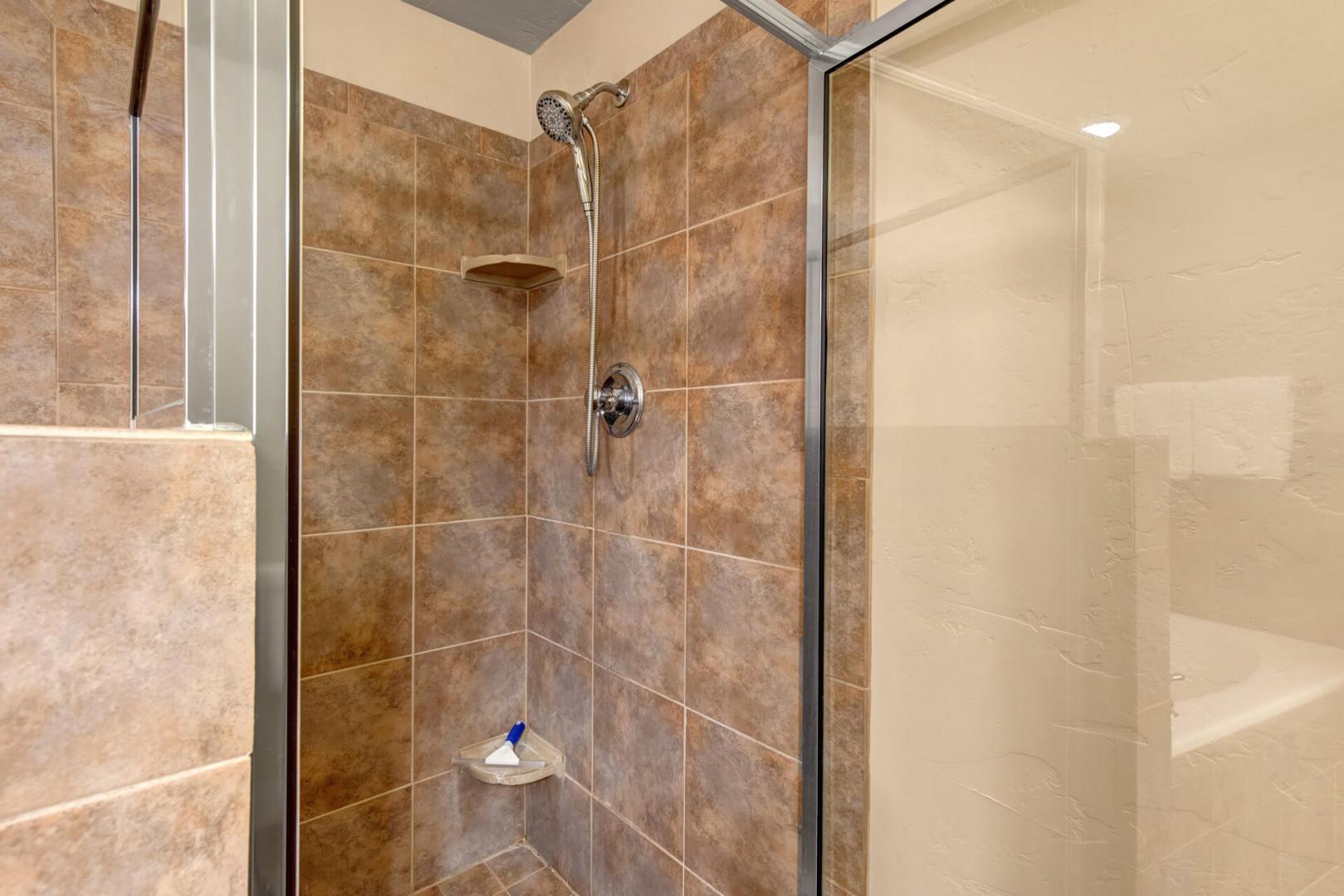Step into your private tiled shower with modern fixtures and a convenient corner shelf for toiletries.