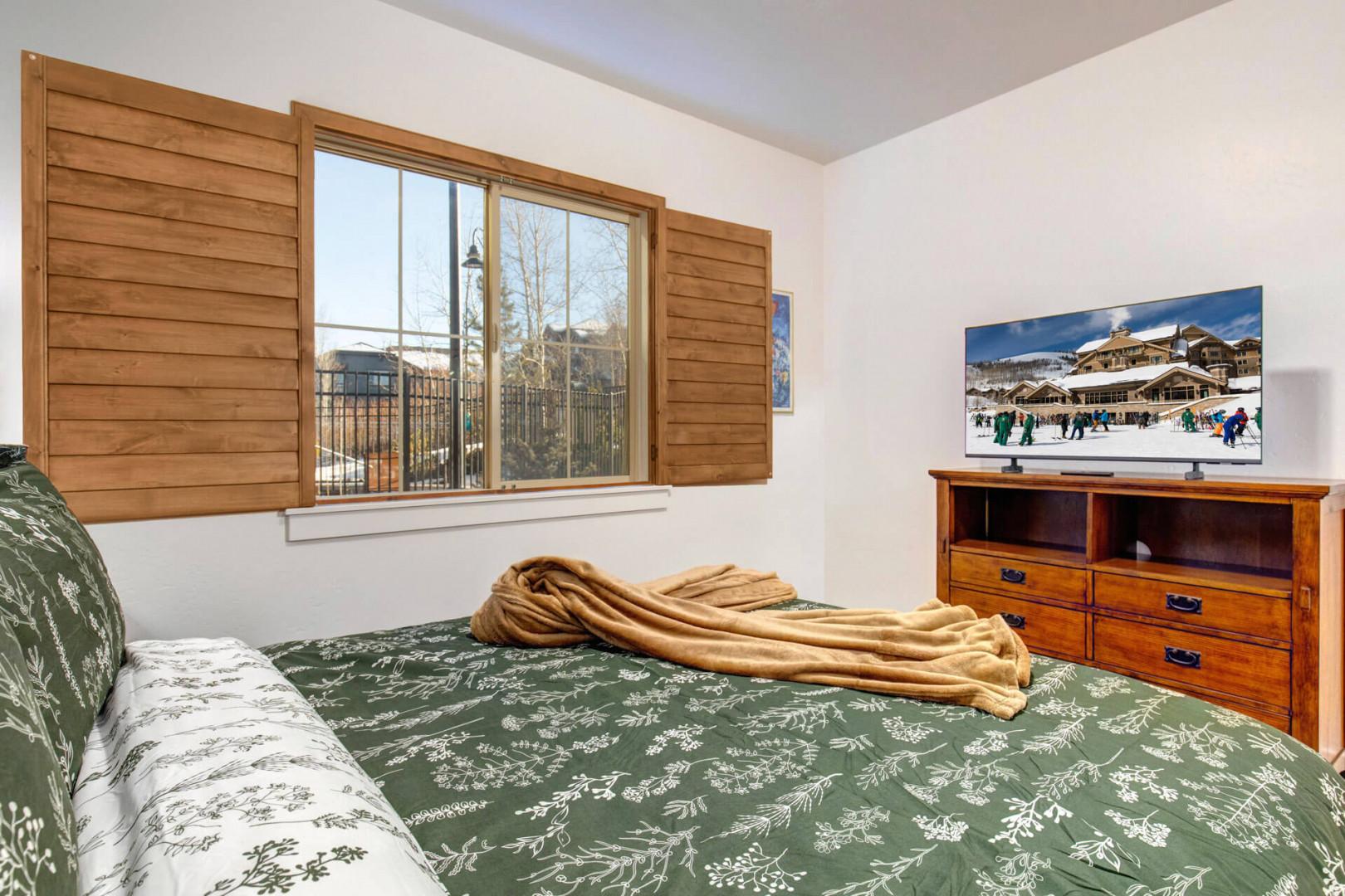 Cozy bedroom with warm wooden shutters, comfortable bedding, and mountain village views perfect for your ski getaway.