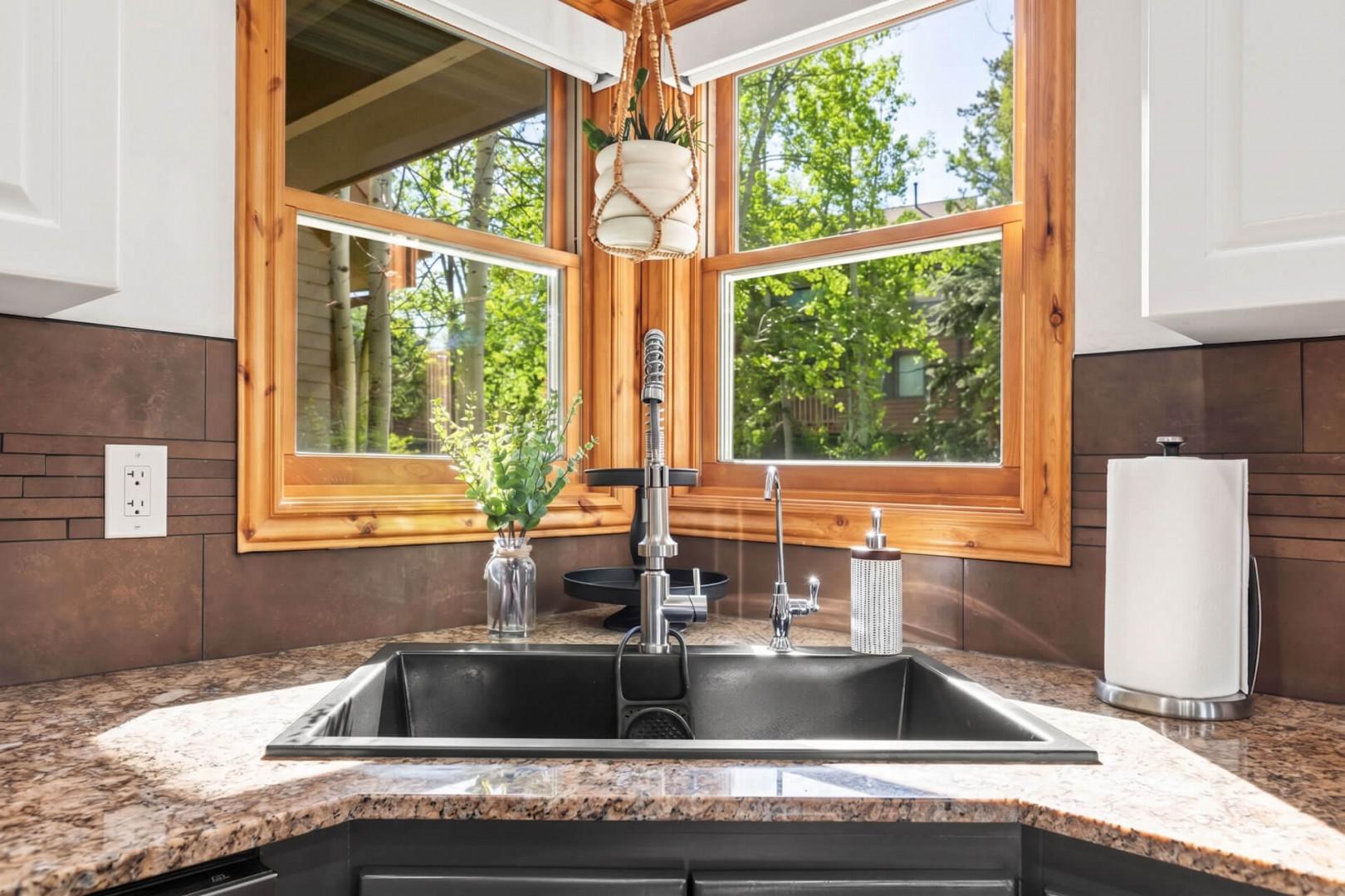 Prepare meals surrounded by natural light streaming through stunning corner windows overlooking lush greenery. This modern kitchen blends rustic wood with sleek finishes for your perfect getaway.