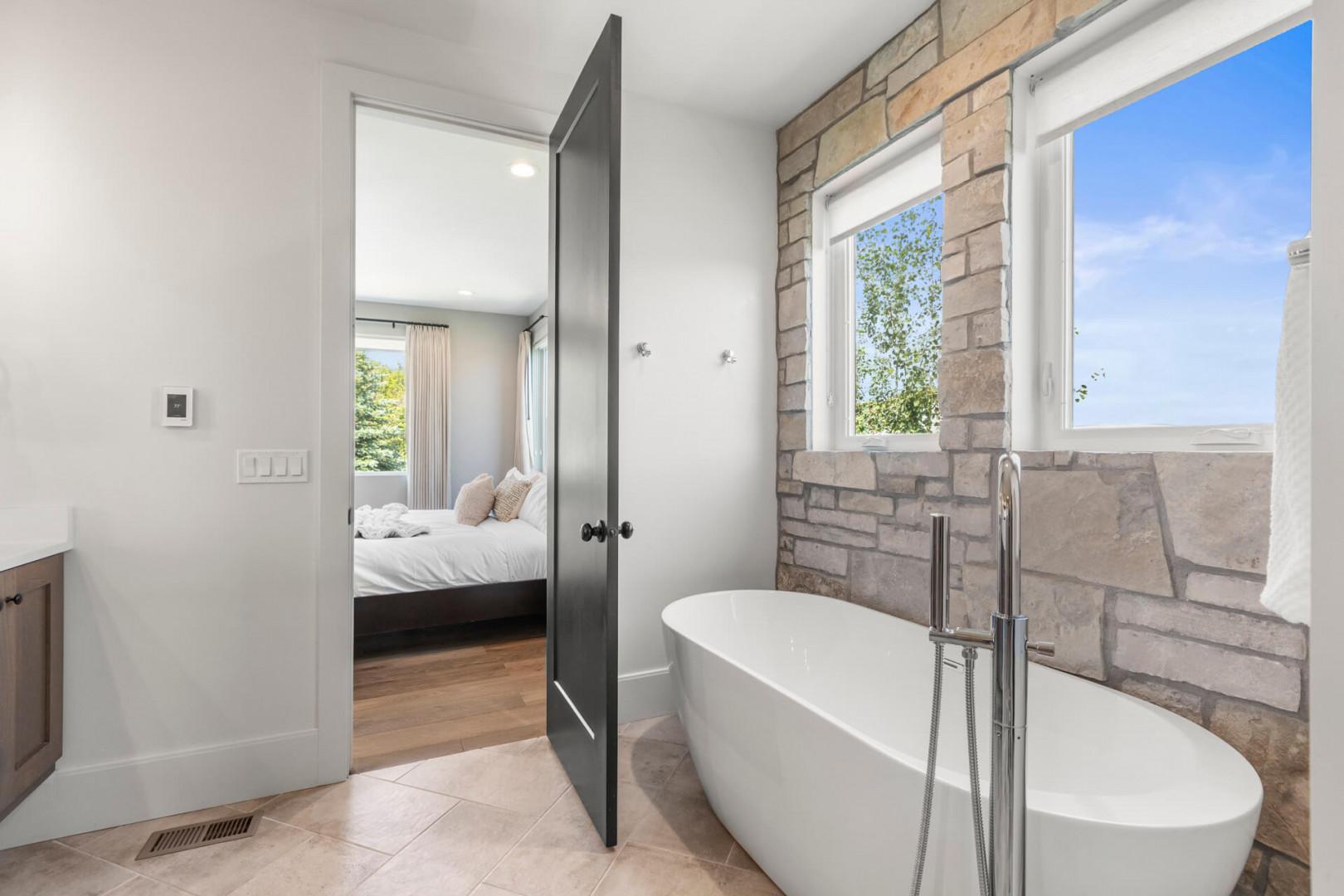 Sink into a luxurious freestanding tub framed by warm stone walls and sunlight streaming through bright windows. Your private spa retreat connects seamlessly to your peaceful bedroom just beyond the door.