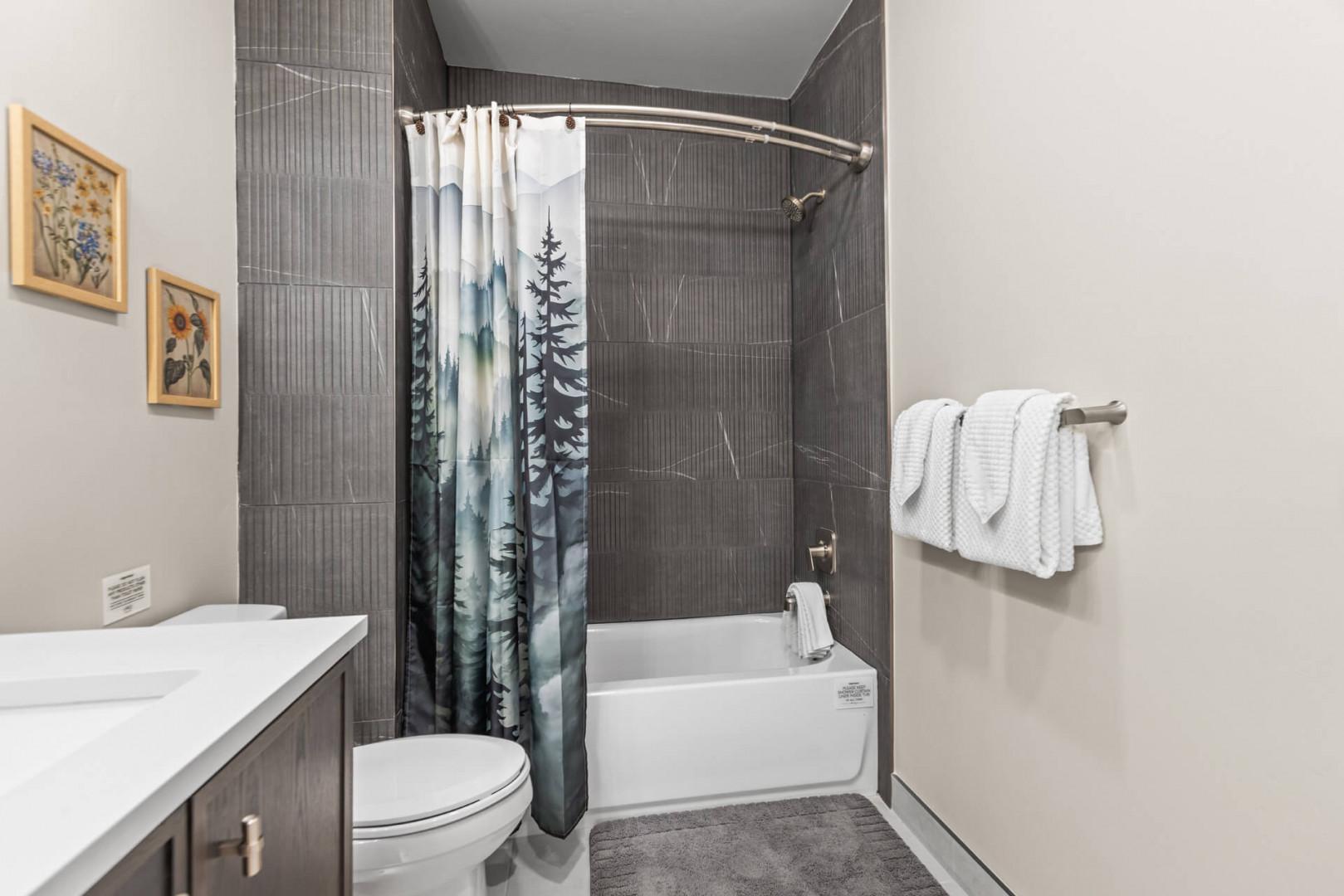 Your private bathroom offers a serene retreat with modern dark tiles, crisp white towels, and a soaking tub perfect for unwinding after exploring.