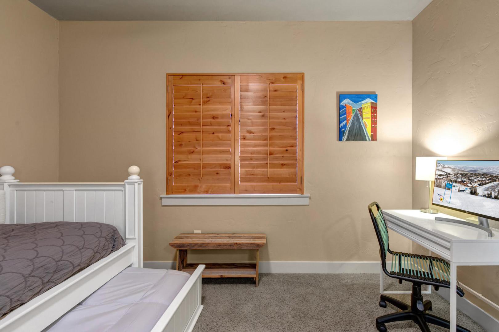 Your cozy bedroom features warm wooden shutters, a comfortable bed, and a dedicated workspace—perfect for both rest and productivity during your stay.