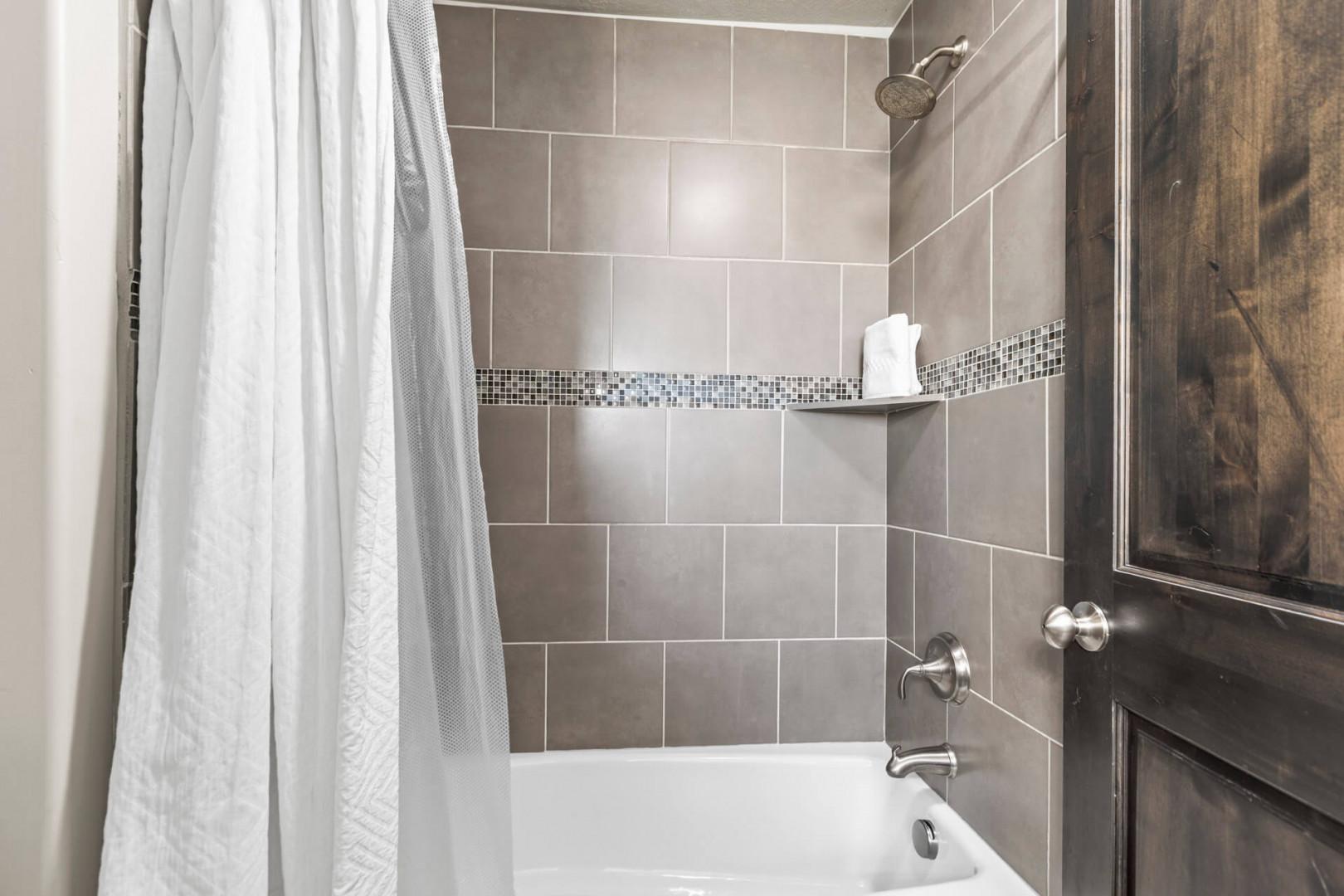 Your private bathroom features elegant gray tile with mosaic accents and a convenient built-in niche for toiletries.
