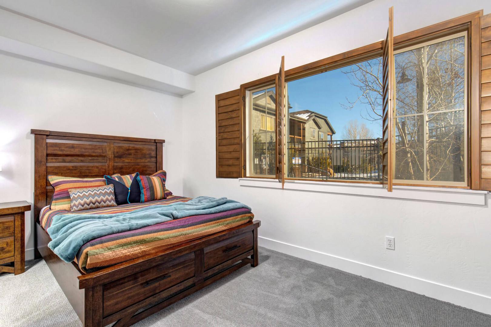 Relax in your cozy primary bedroom featuring a Queen bed with vibrant linens and natural light streaming through charming wood shutters.