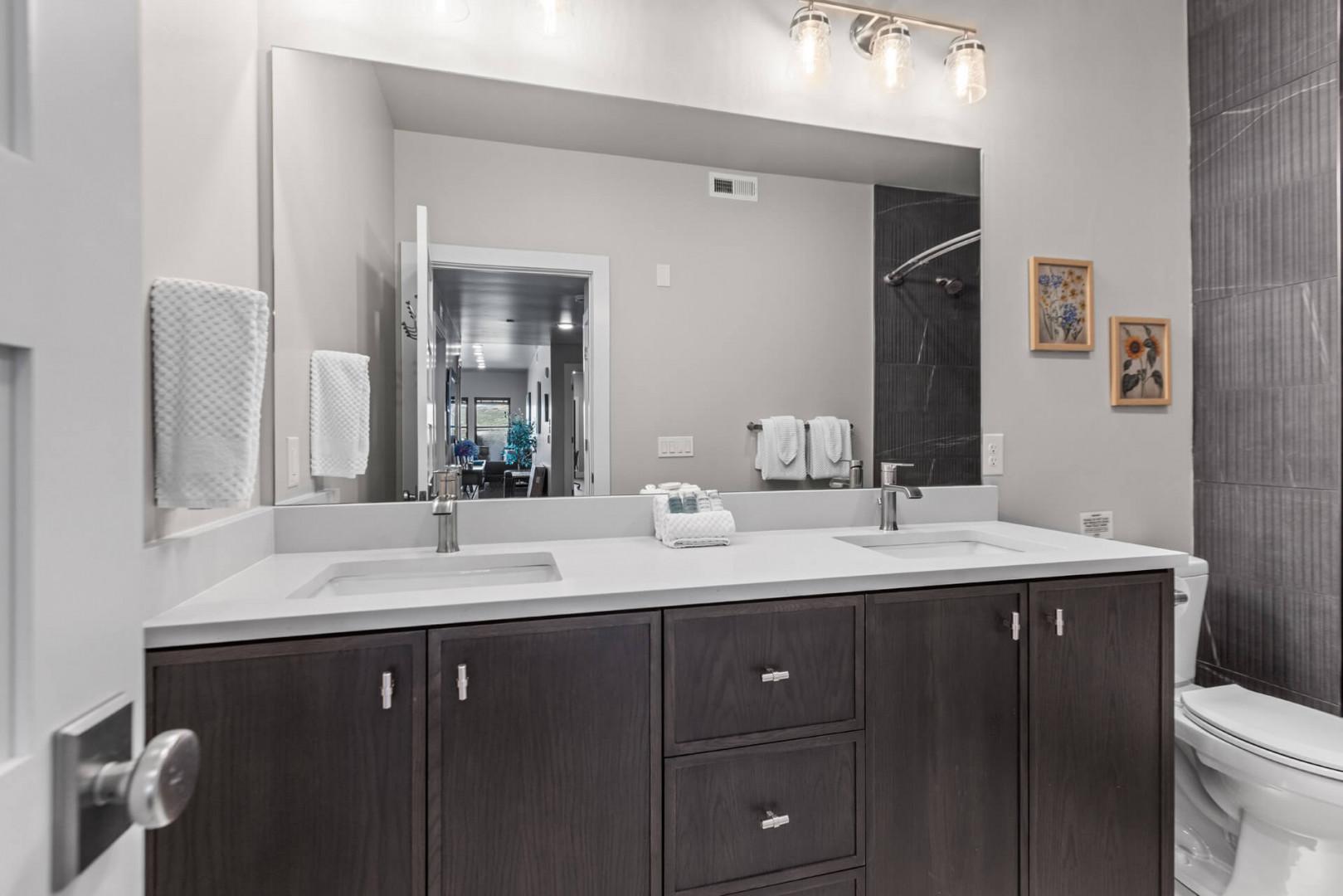 Freshen up in your modern bathroom with dual sinks, sleek dark cabinetry, and a spacious walk-in shower with elegant tile details.
