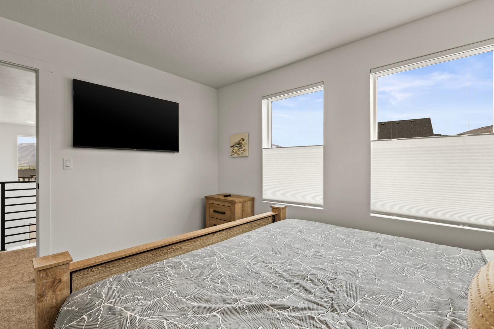 Your bright bedroom features a wall-mounted TV and peaceful windows for restful mornings and cozy evenings.