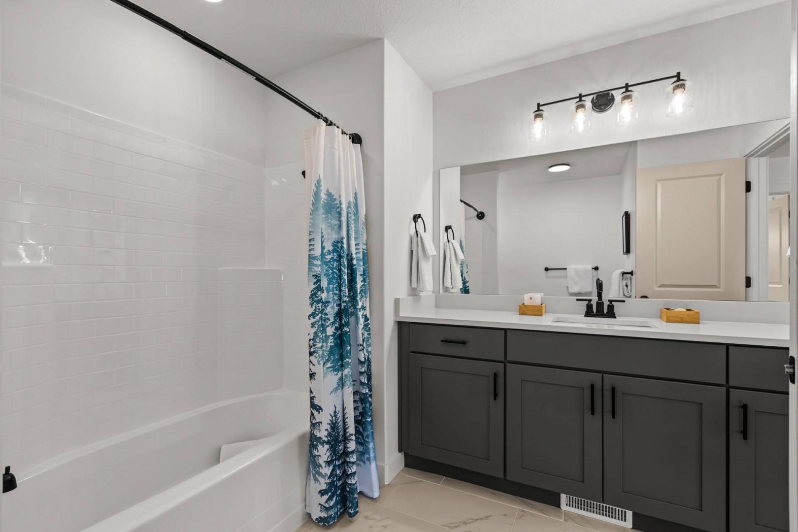 Unwind in your spacious bathroom with crisp white subway tiles, forest-themed curtains, and modern gray cabinetry creating a spa-like retreat.